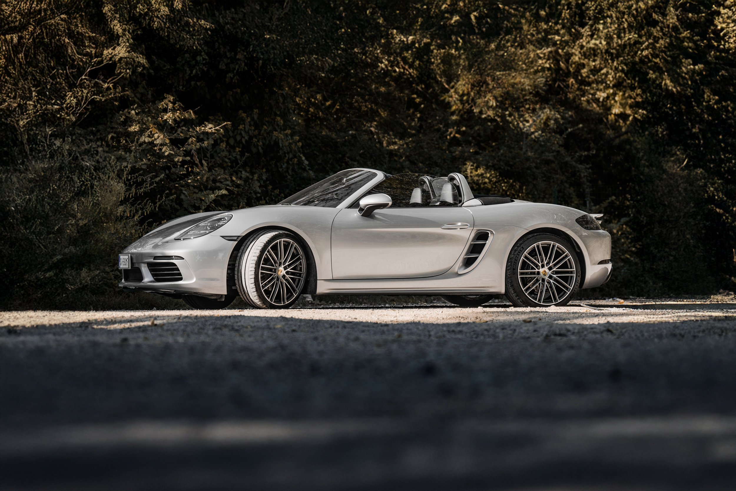 Auto sportiva Porsche cabriolet grigia parcheggiata su una strada con sfondo di alberi autunnali.