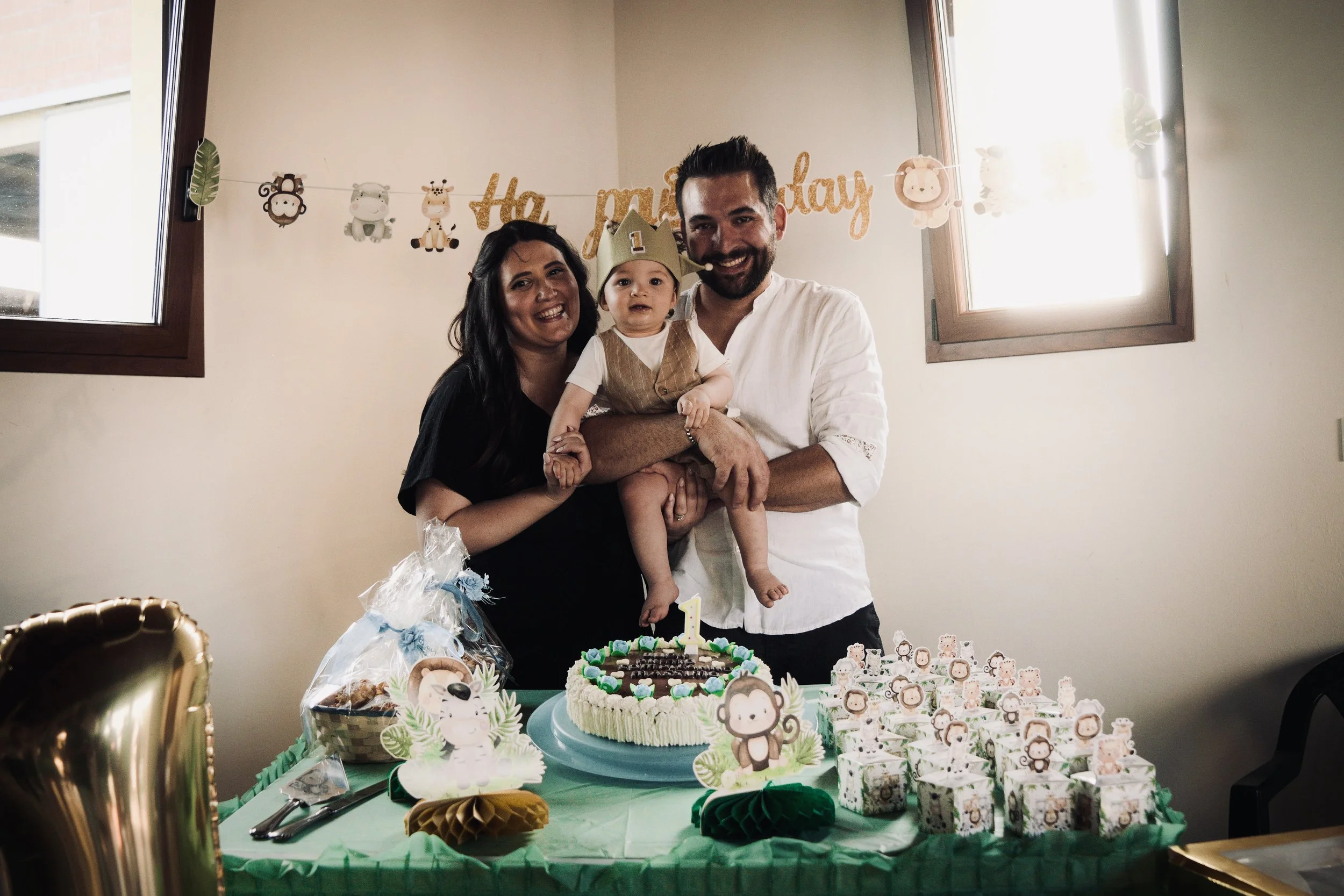 Una famiglia felice con un bambino in occasione del suo primo compleanno, con torta decorata e regali sulla tavola, all'interno di una stanza con decorazioni per bambini.