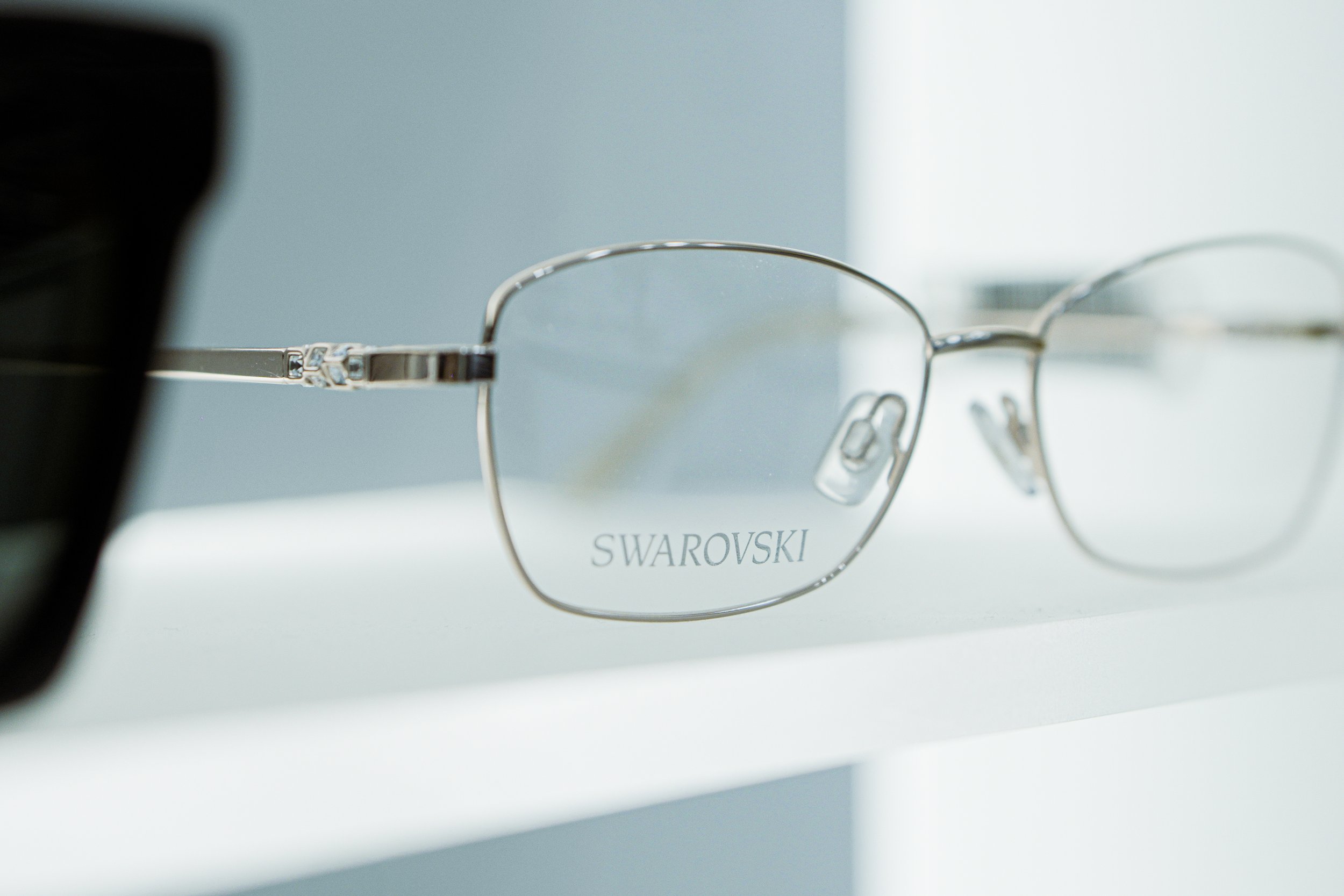 Occhiali da vista con montatura in metallo inciso con la scritta 'SWAROVSKI' appoggiati su una superficie bianca