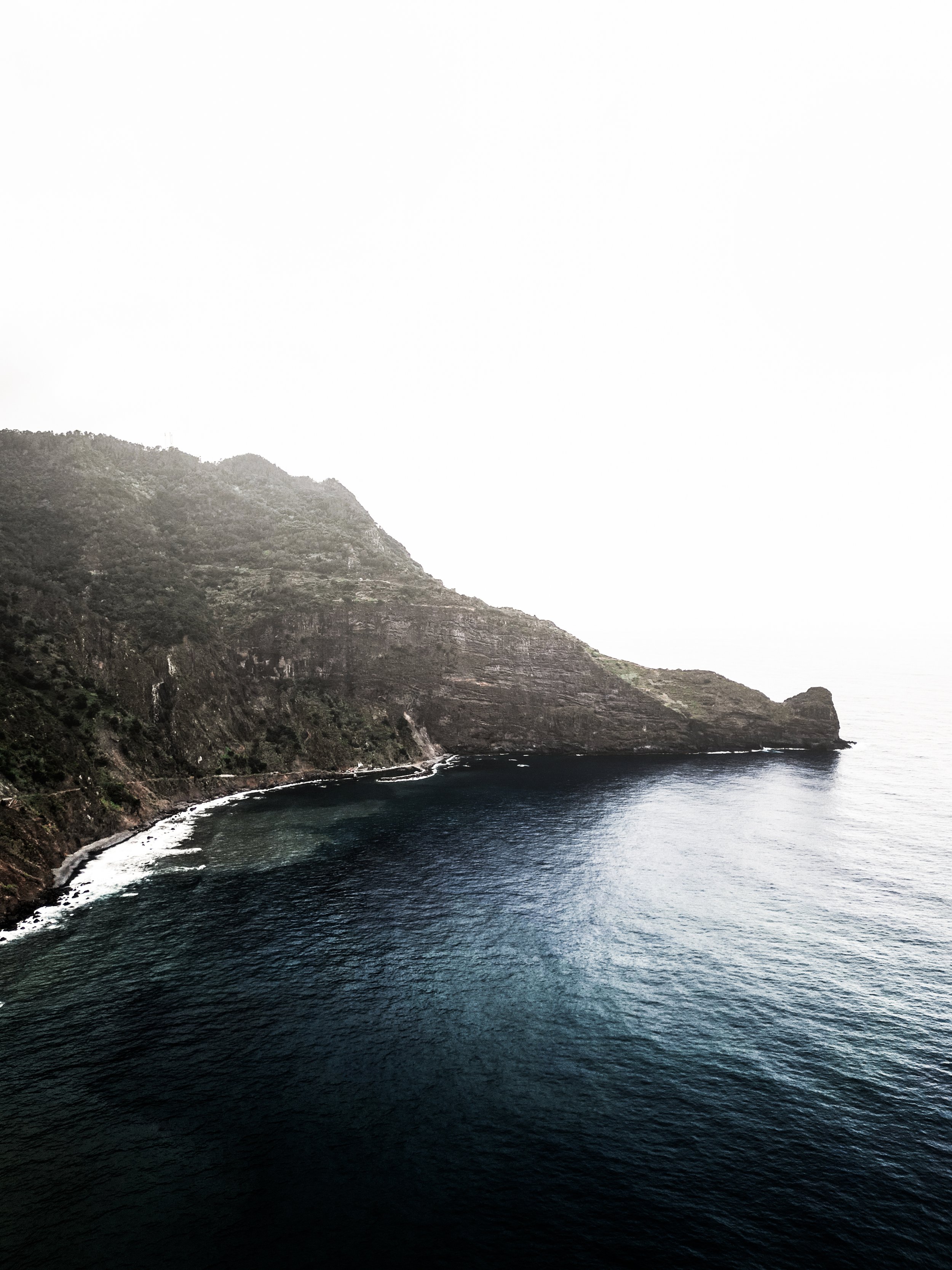 Costa rocciosa e marina, con onde che si infrangono sulla spiaggia e montagne verdi sullo sfondo.