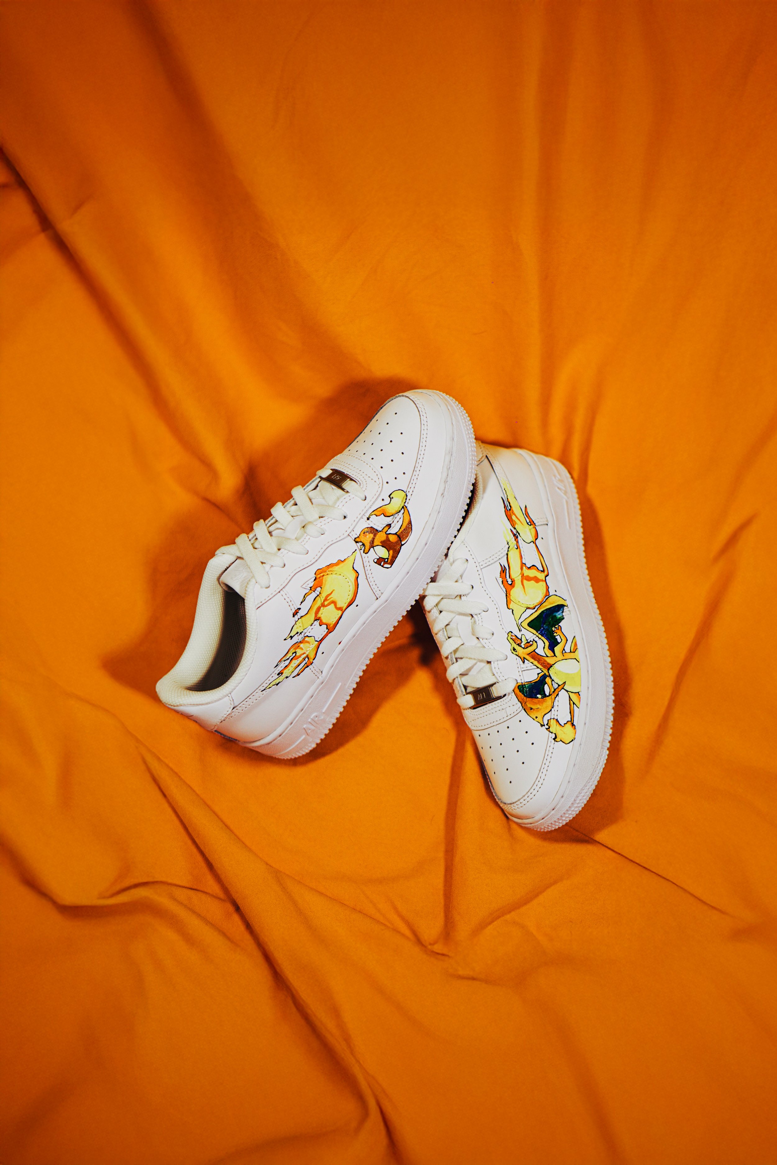 Scarpe da ginnastica bianche con disegni di figure gialle e arancioni, posizionate su una sedia di tessuto arancione