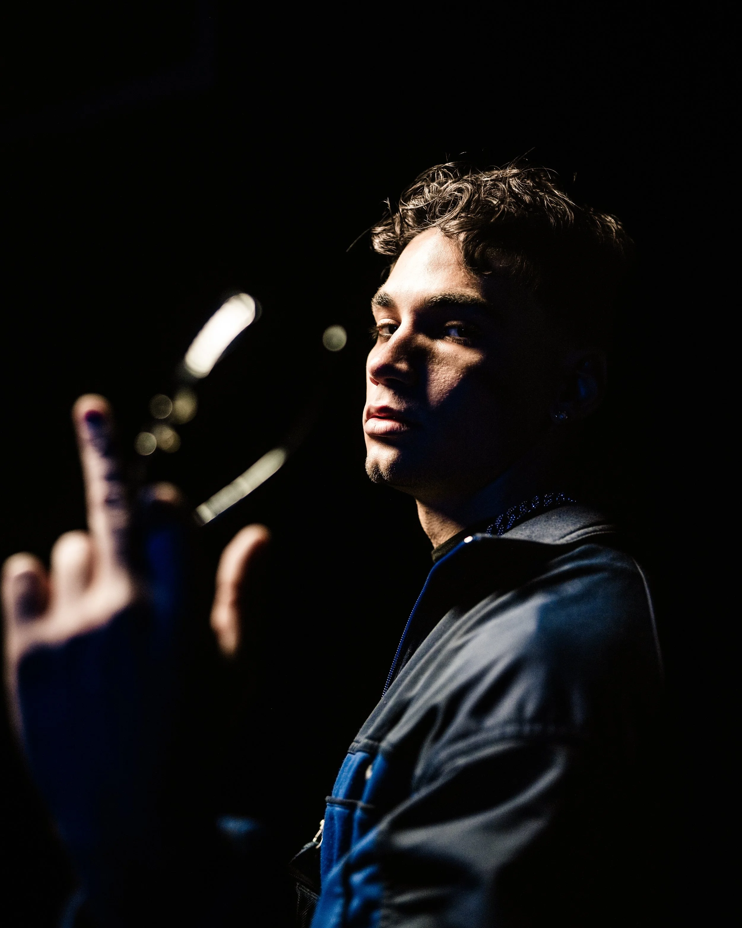 Ragazzo in abbigliamento sportivo con sfondo nero, che guarda verso la fotocamera e fa un gesto con quattro dita