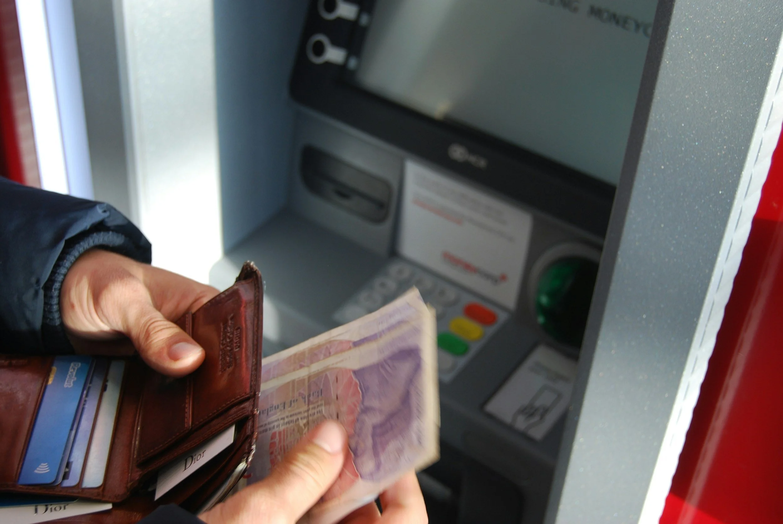 Person holding a wallet and cash at an ATM machine.