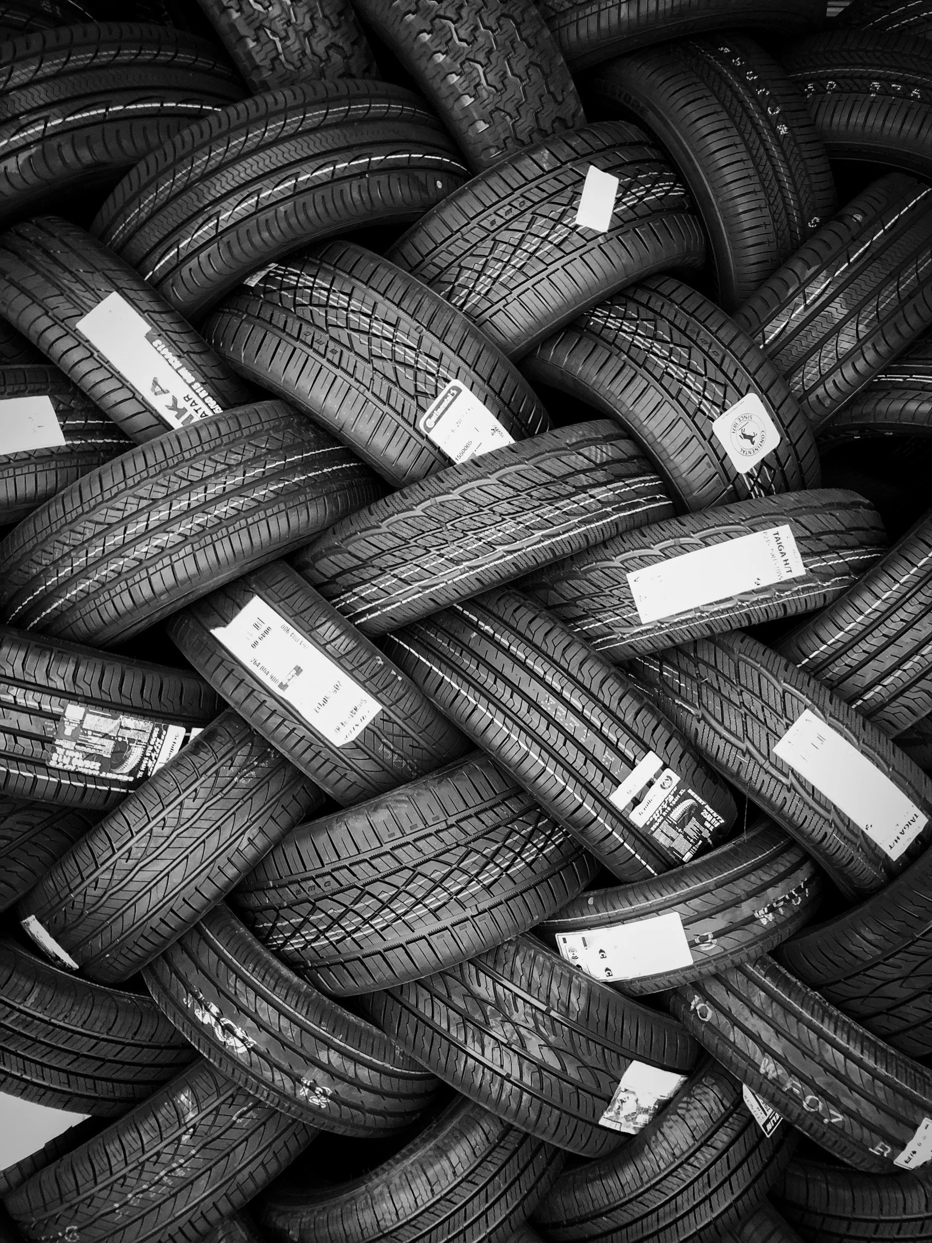 A large pile of stacked and intertwined black car tires with white labels.