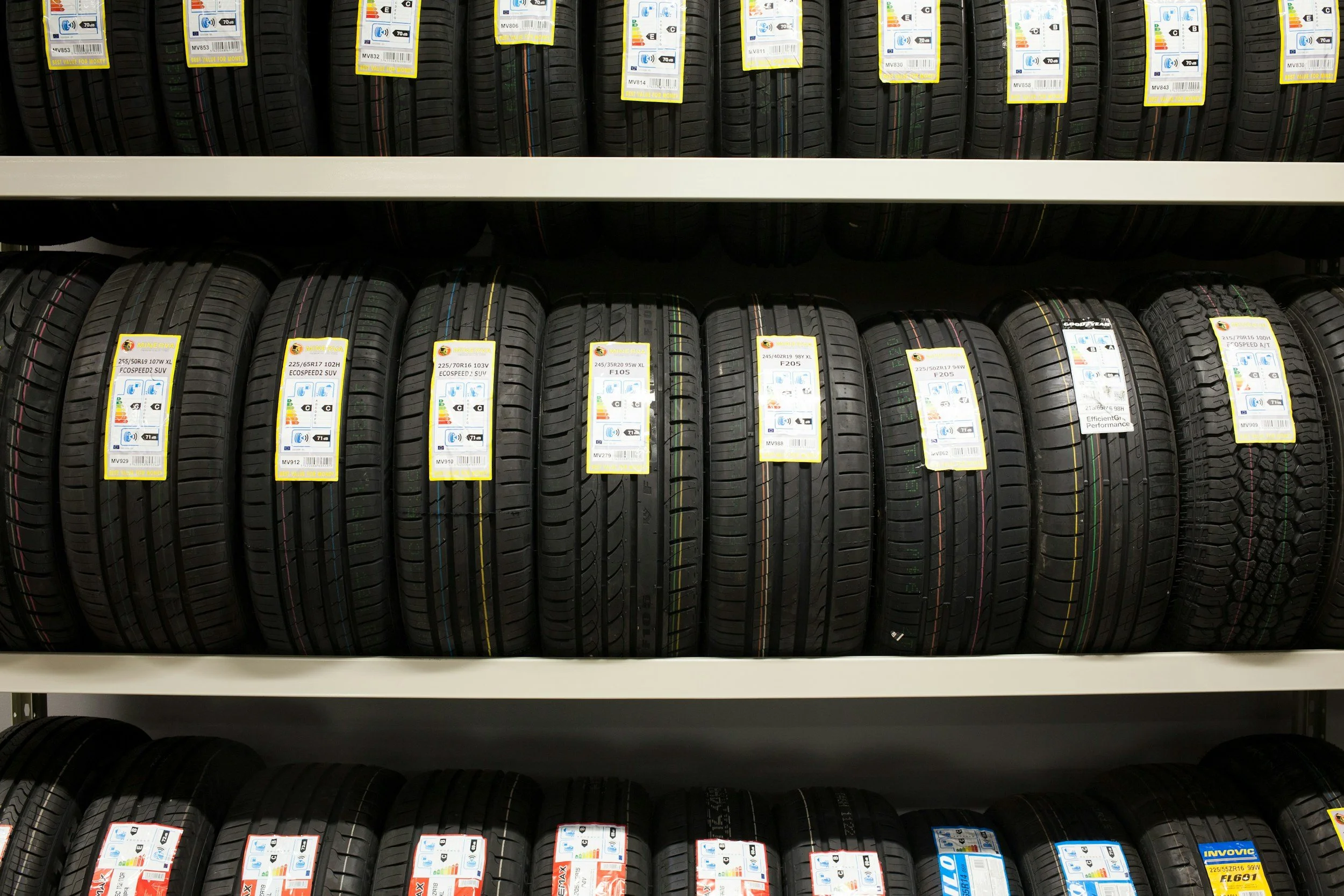 Stacked shelves of new tires with labels displaying size and specifications in a tire store.