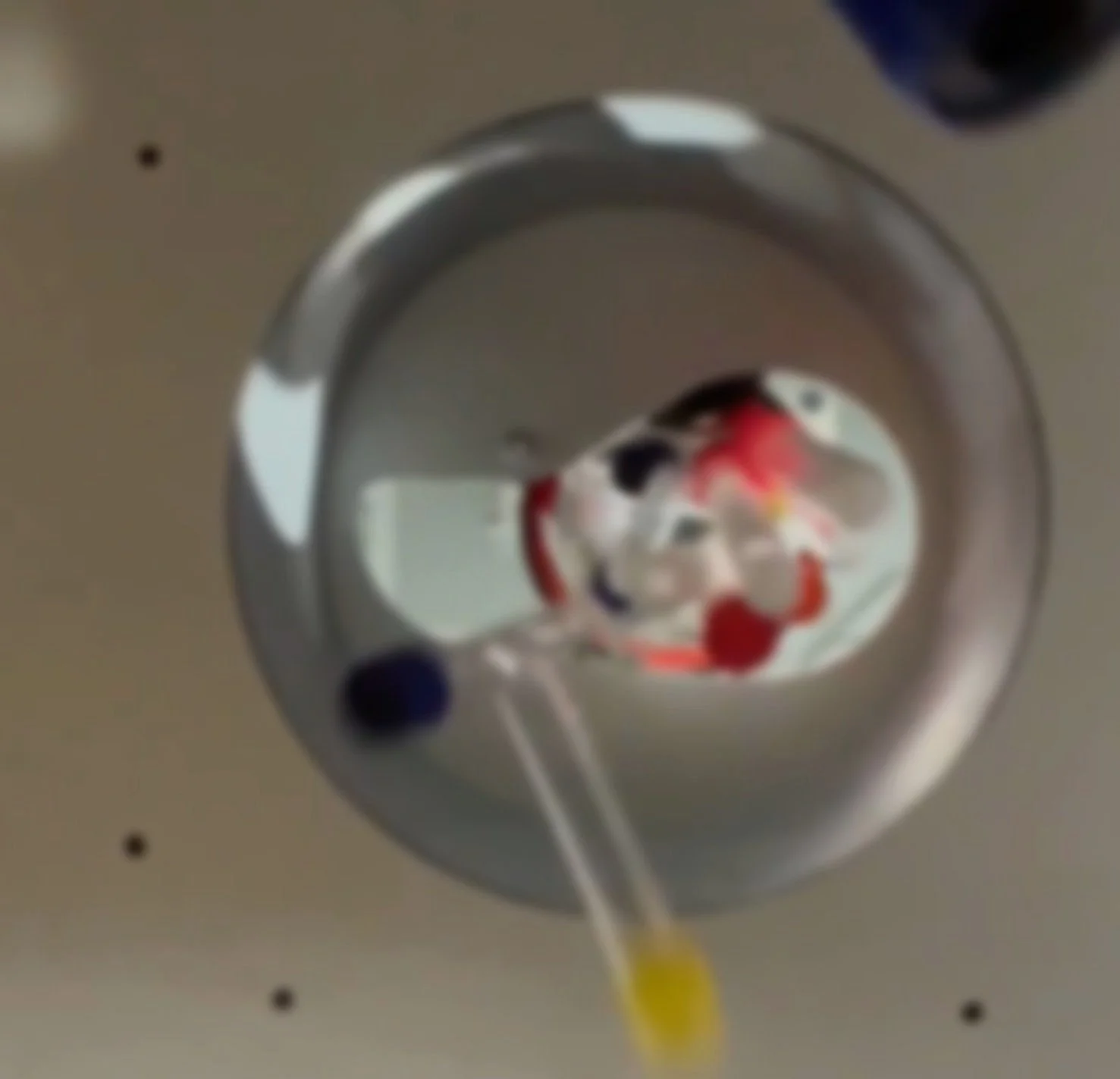 Reflected image of a person wearing a hat using a mirror on a ceiling, with a straw and yellow liquid in the foreground.