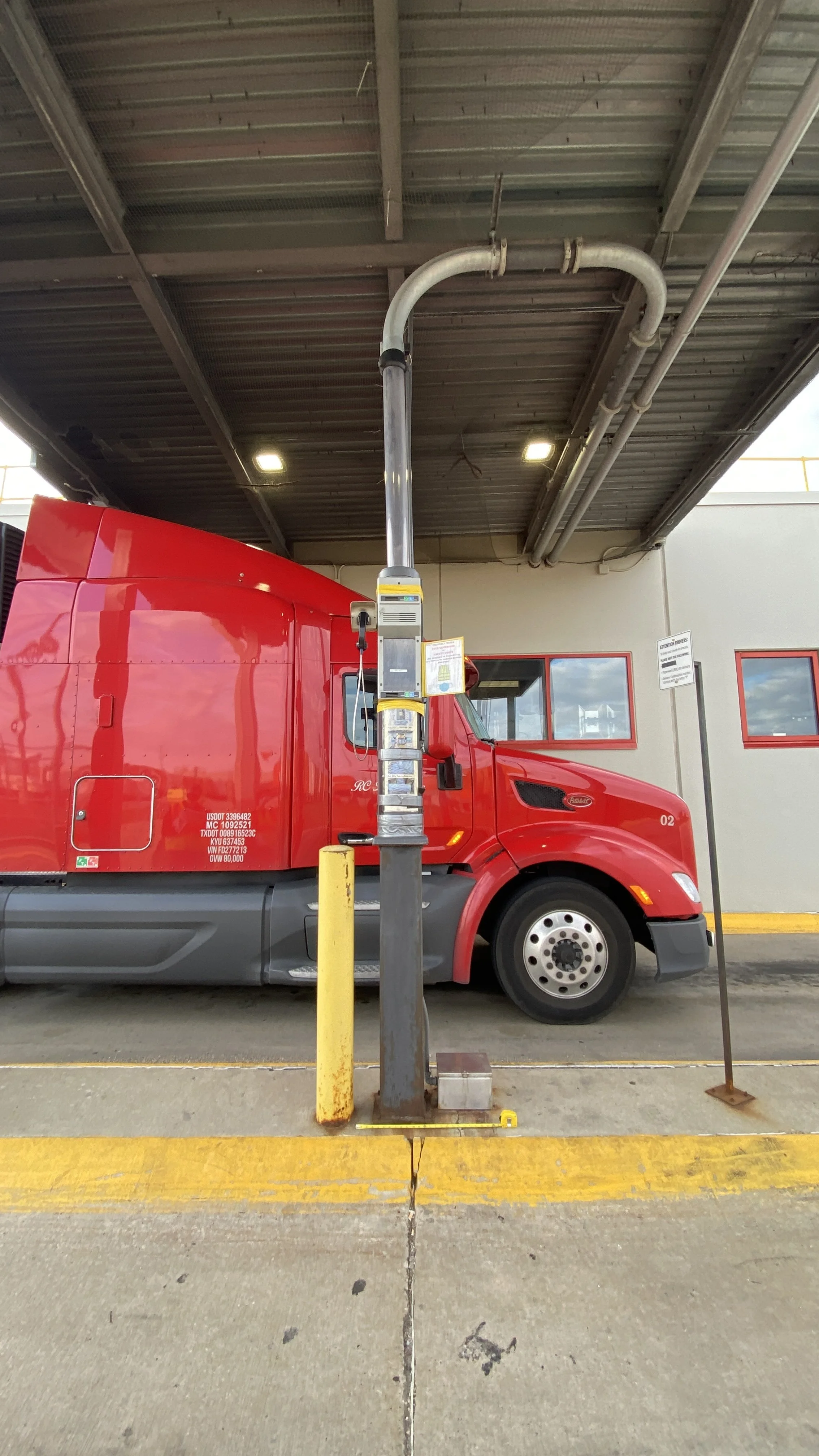 Red semi-truck parked under a canopy with a fueling station in front of it.