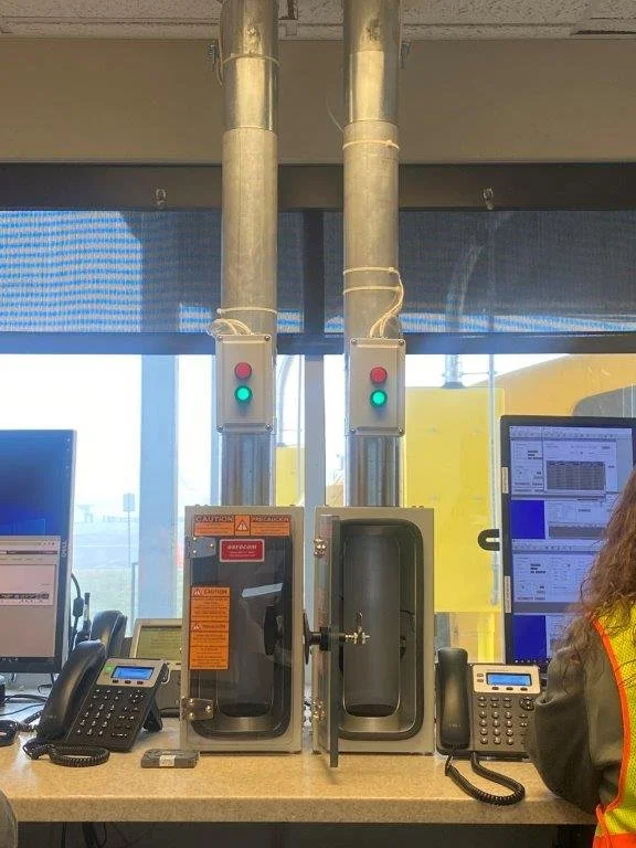Two tower systems with red and green indicator lights and safety signs, placed between computer monitors, in an office or control room setting.