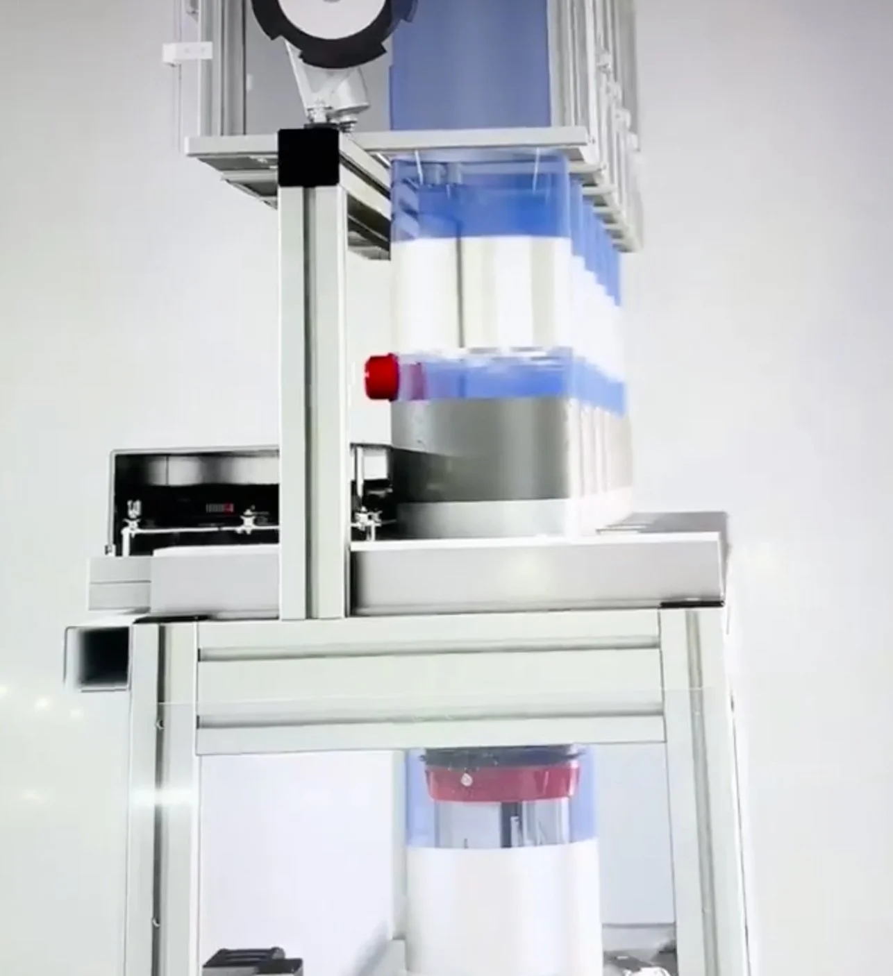 Automated machine with transparent containers, metal frame, and red and black components, used in pharmaceutical or medical manufacturing.