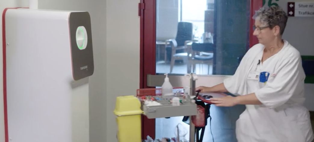 Medical staff using disinfectant cart in a clinical setting with a hand sanitizer dispenser on the wall.