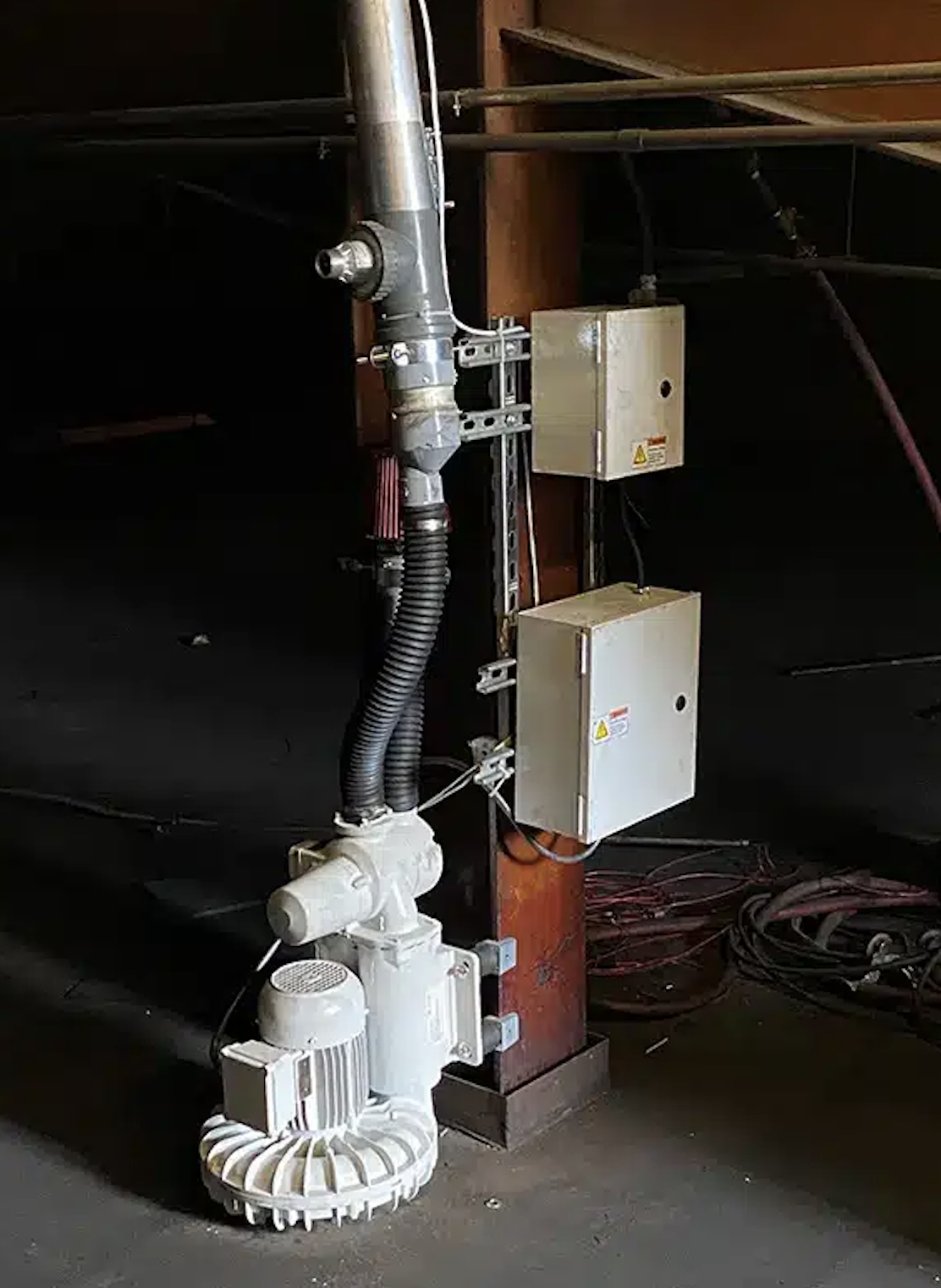 Industrial machinery with pipes, wires, and electrical boxes mounted on a wooden beam in a dimly lit space.