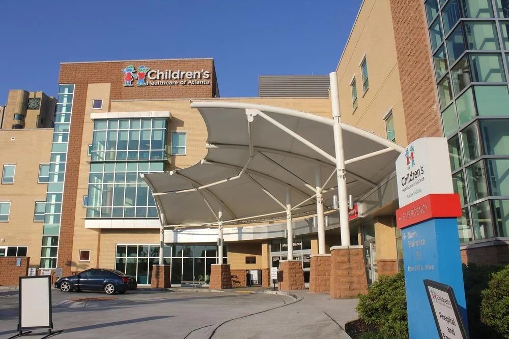Children’s Healthcare of Atlanta hospital entrance with a large white canopy and a sign indicating emergency and main entrance.