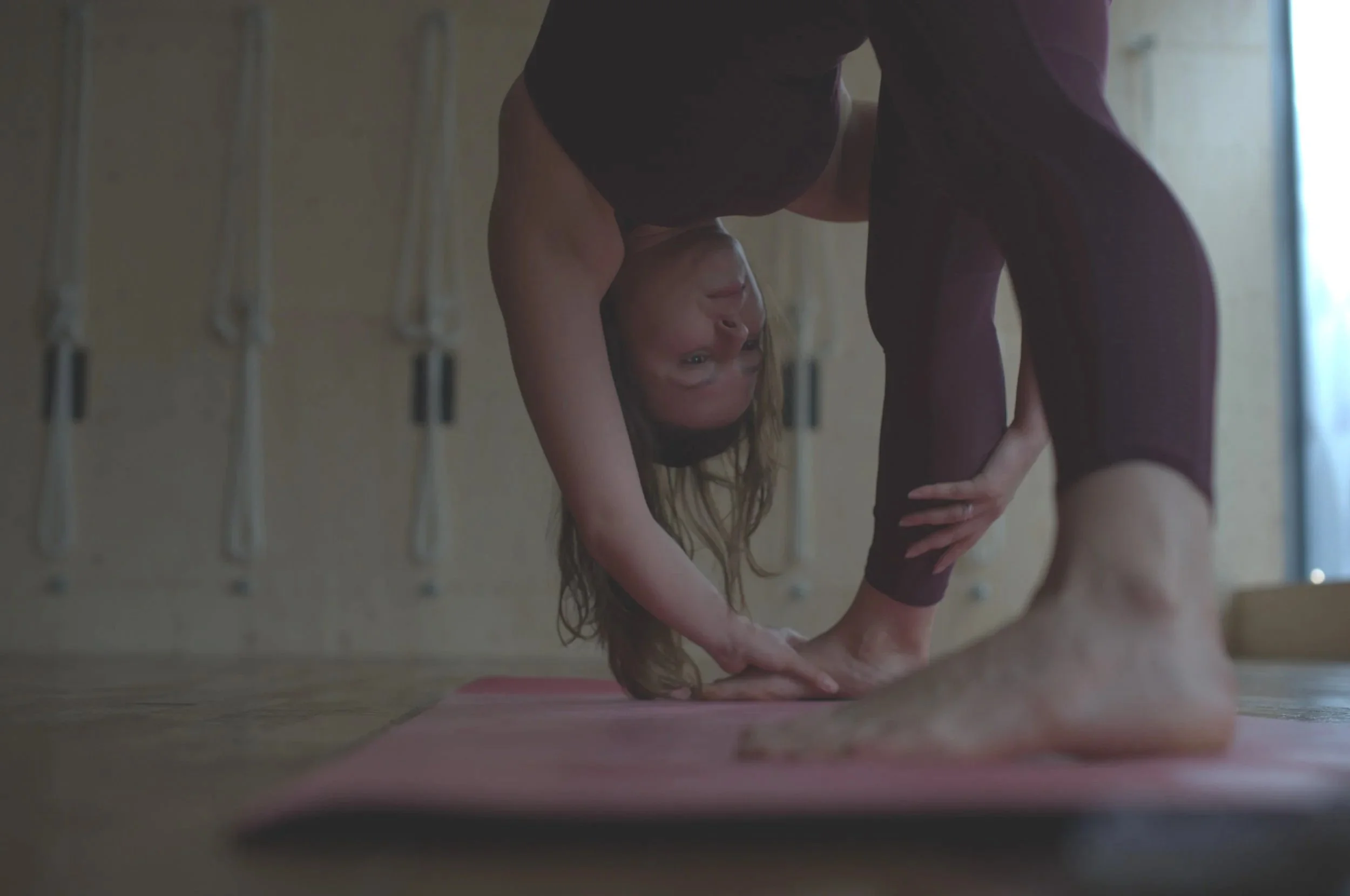 Person performing a headstand yoga pose on a pink mat in a studio.