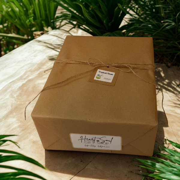 A brown gift box wrapped with string and labeled 'Heart & Soul Gift Shop' and 'Tropical Oasis' on a sandy surface surrounded by green plants.