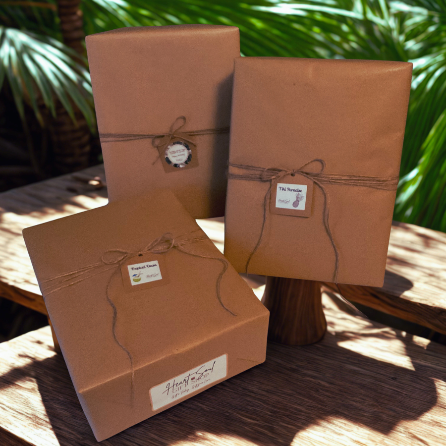 Three brown paper packages tied with string, placed on a wooden table with green tropical plants in the background.