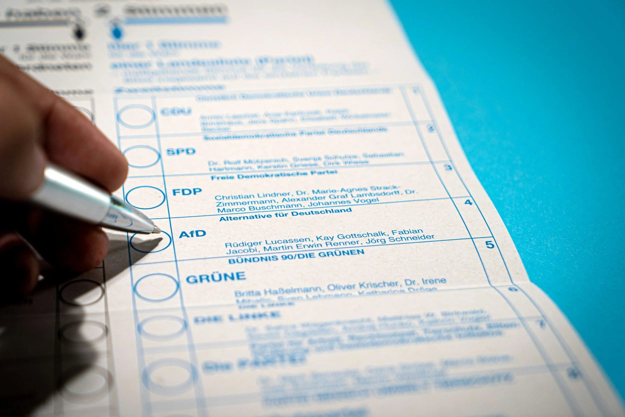 A person filling out a ballot paper with a pen, in an election setting.