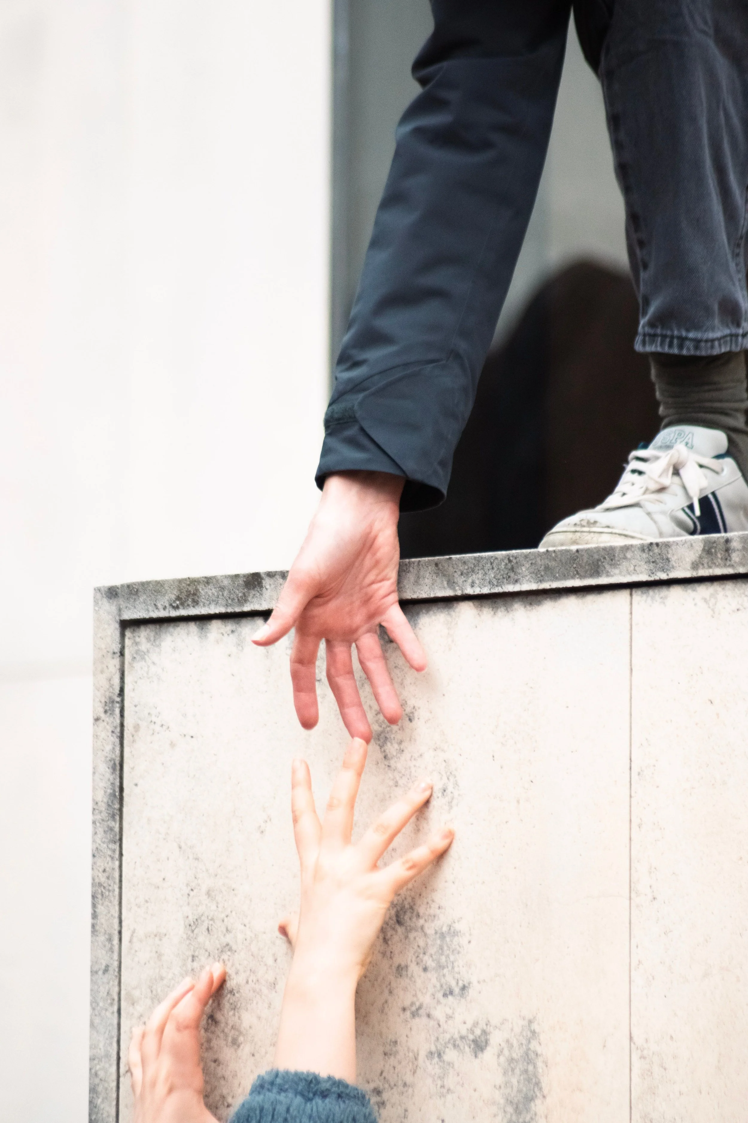 A person's hand reaching down from above with fingers extended towards a person's hand reaching up from below, all over a stone surface.