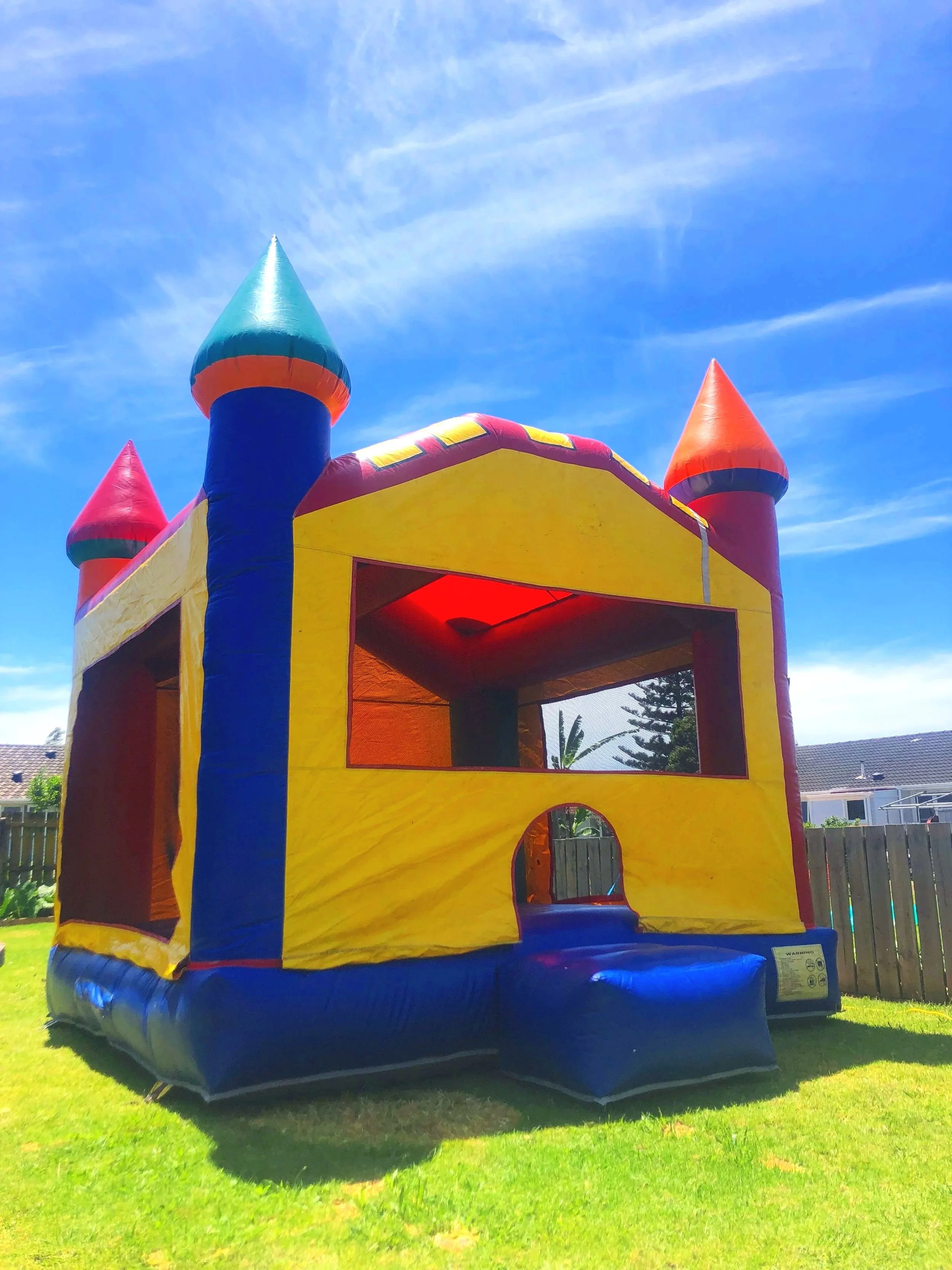 Colorful inflatable bounce house with Mickey Mouse and Minnie Mouse figures on top, slide on the right side, set up in a backyard.