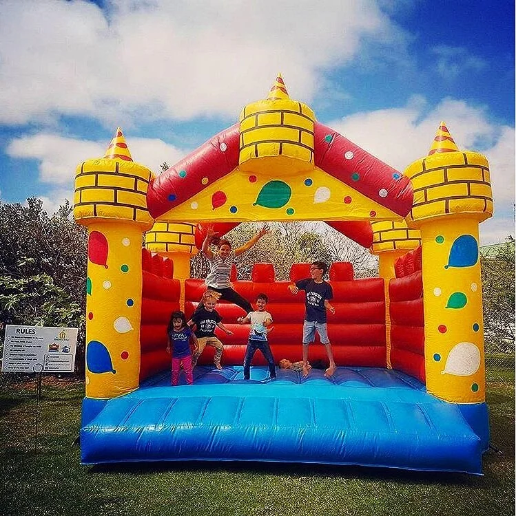Children playing on a colorful inflatable bounce house shaped like a castle with yellow, red, blue, and green decorations outdoors.