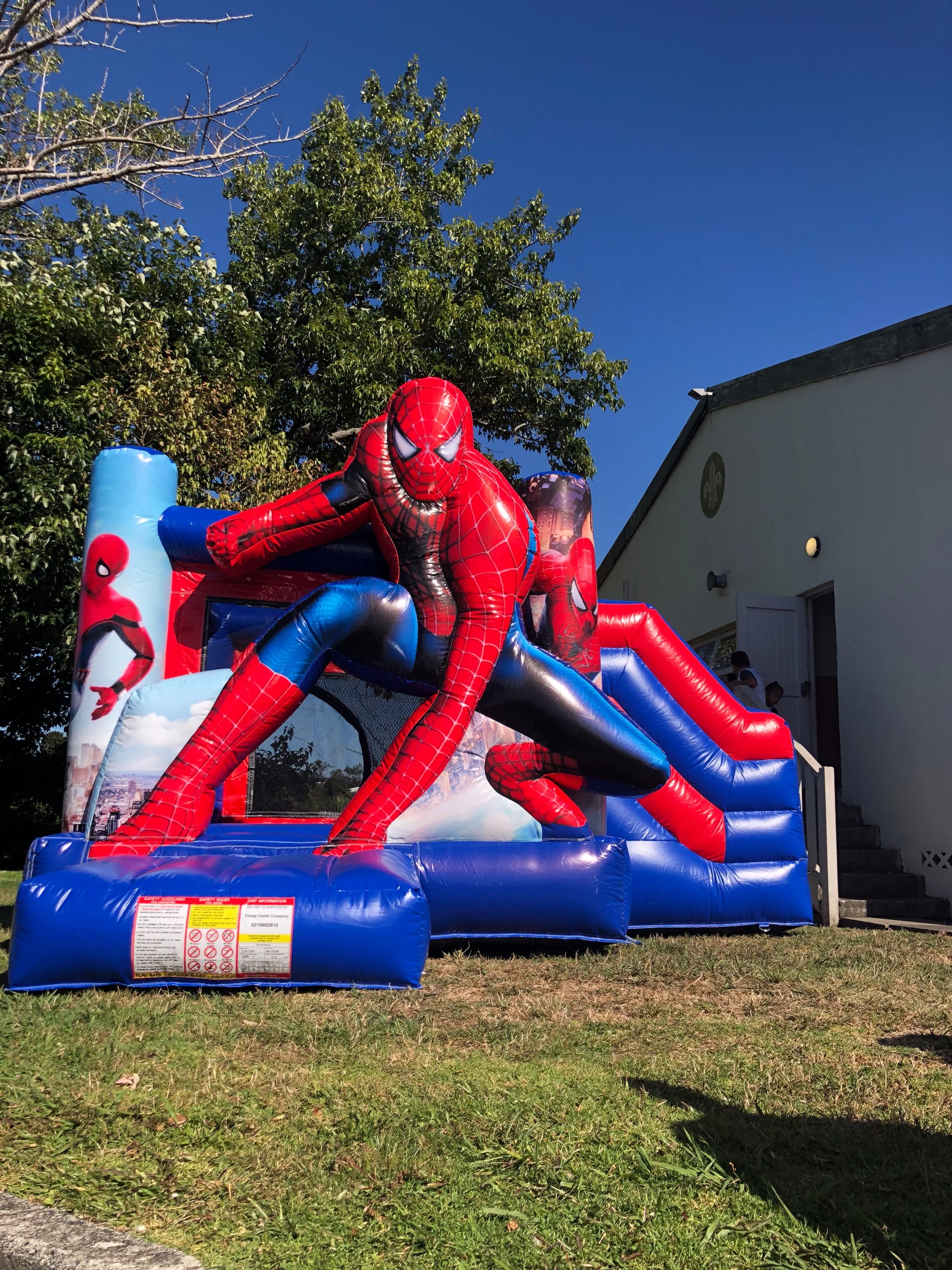 Colorful inflatable bounce house designed to look like a castle, with yellow, red, and blue sections, set up outdoors on artificial grass.
