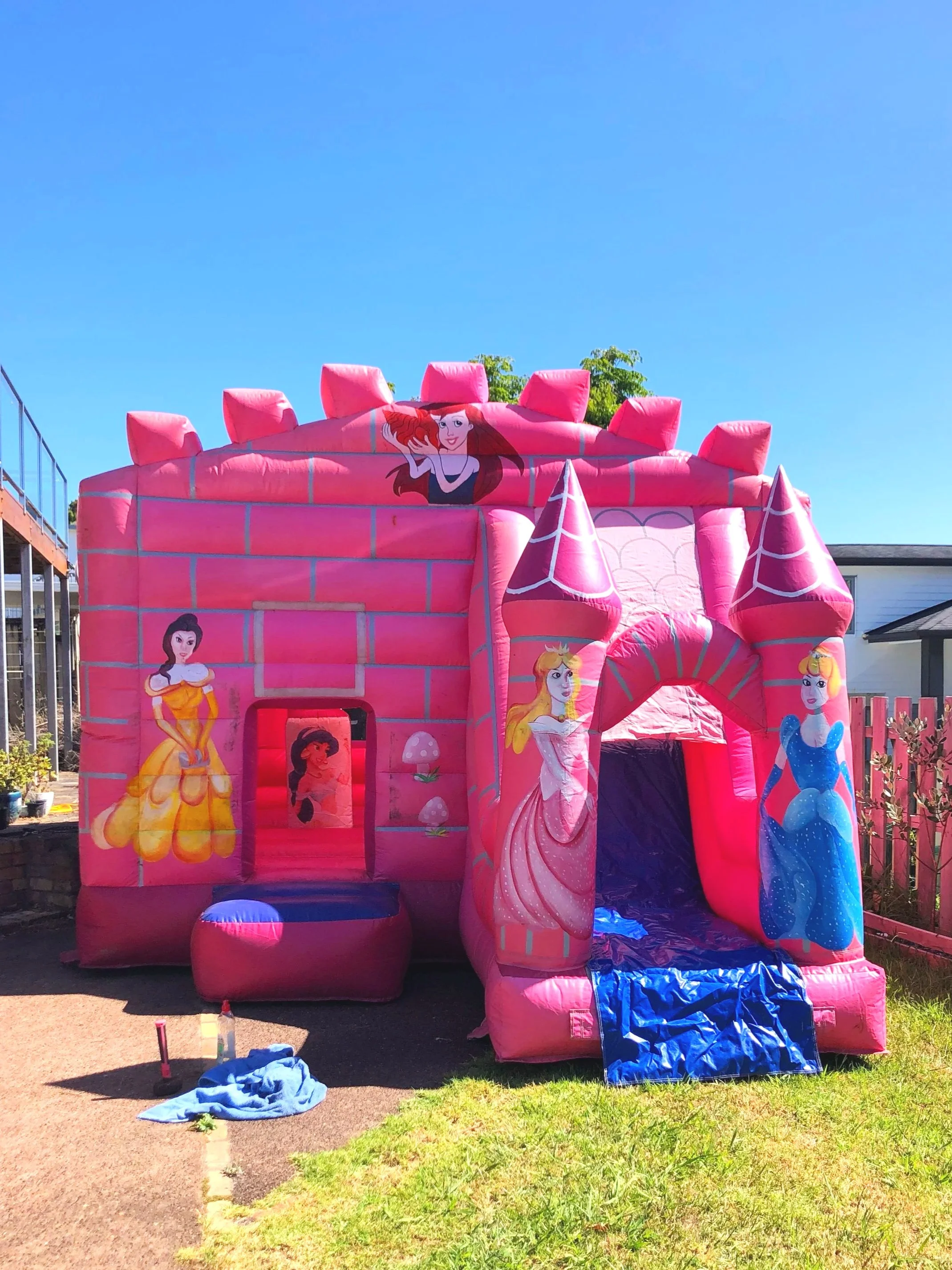 Children playing on a colorful inflatable castle with a yellow and red theme, resembling a castle with towers, outdoors on a grassy area under a partly cloudy sky.