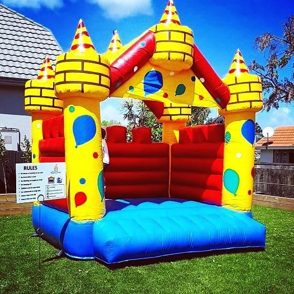 Brightly colored inflatable bounce house resembling a castle with yellow, red, and blue colors, set up outdoors on a grassy yard with houses and trees in the background.