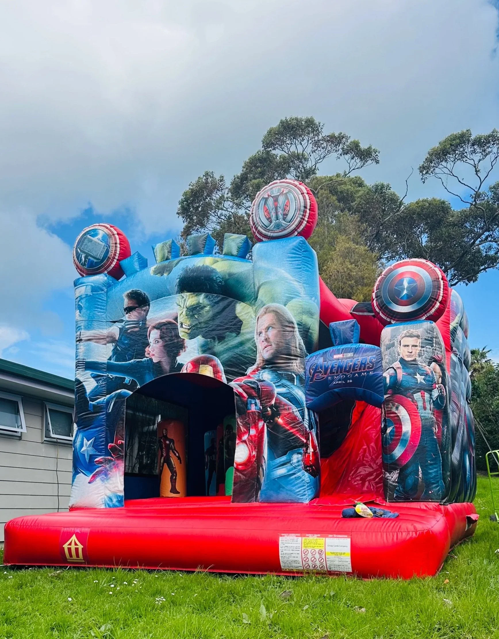 Colorful inflatable castle with turrets resembling a castle, set up on a grassy yard with houses and trees in the background.