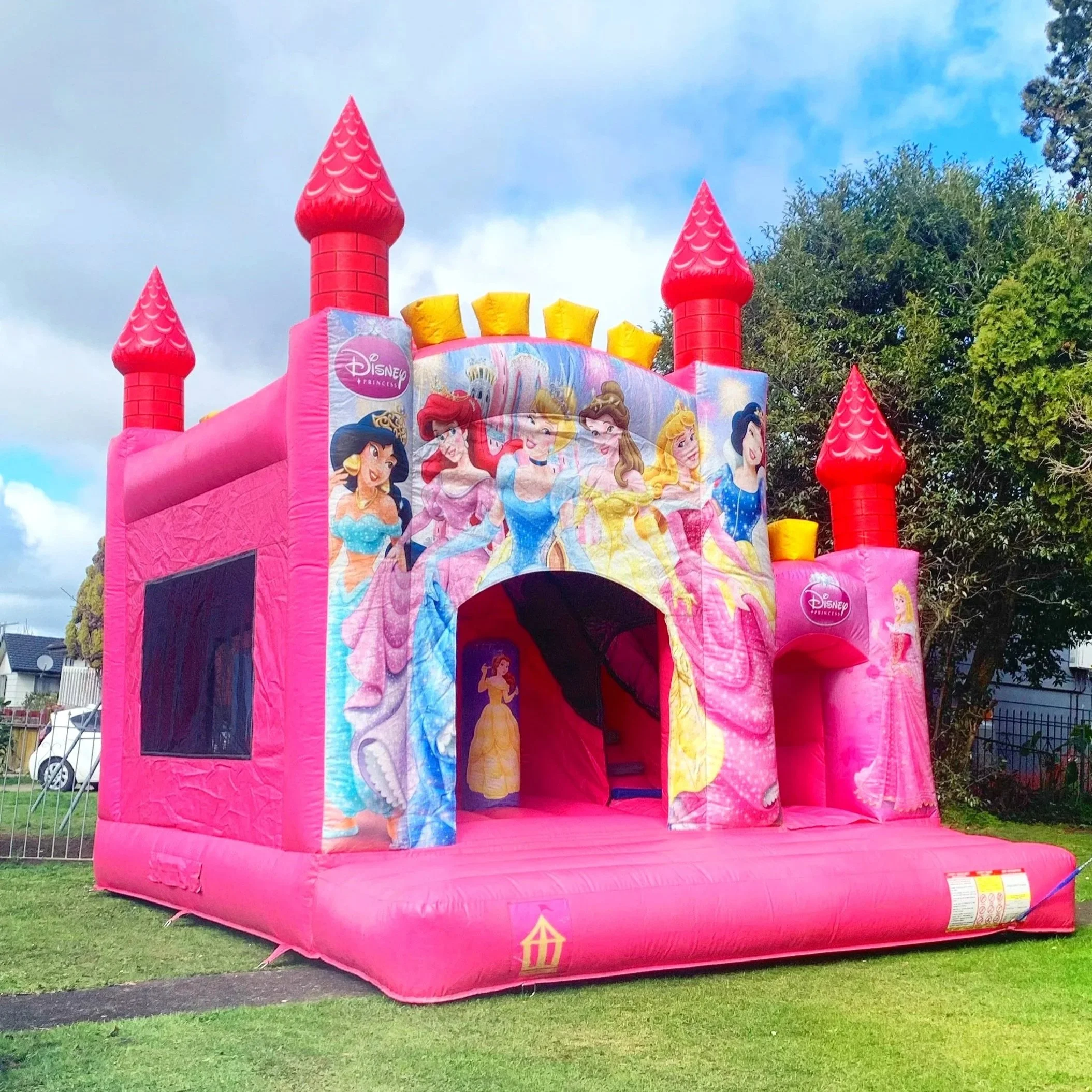 Colorful inflatable bounce house shaped like a castle with yellow turrets, blue walls, and a red slide on a residential driveway.