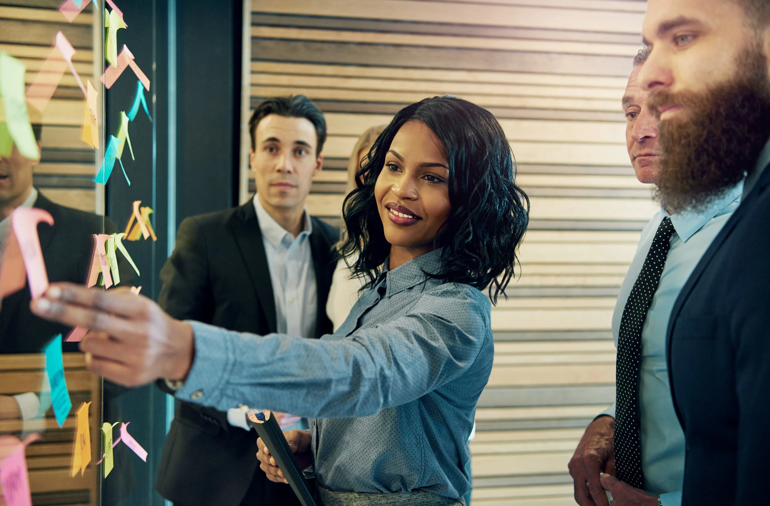 Group of professionals in a meeting using sticky notes on glass wall.
