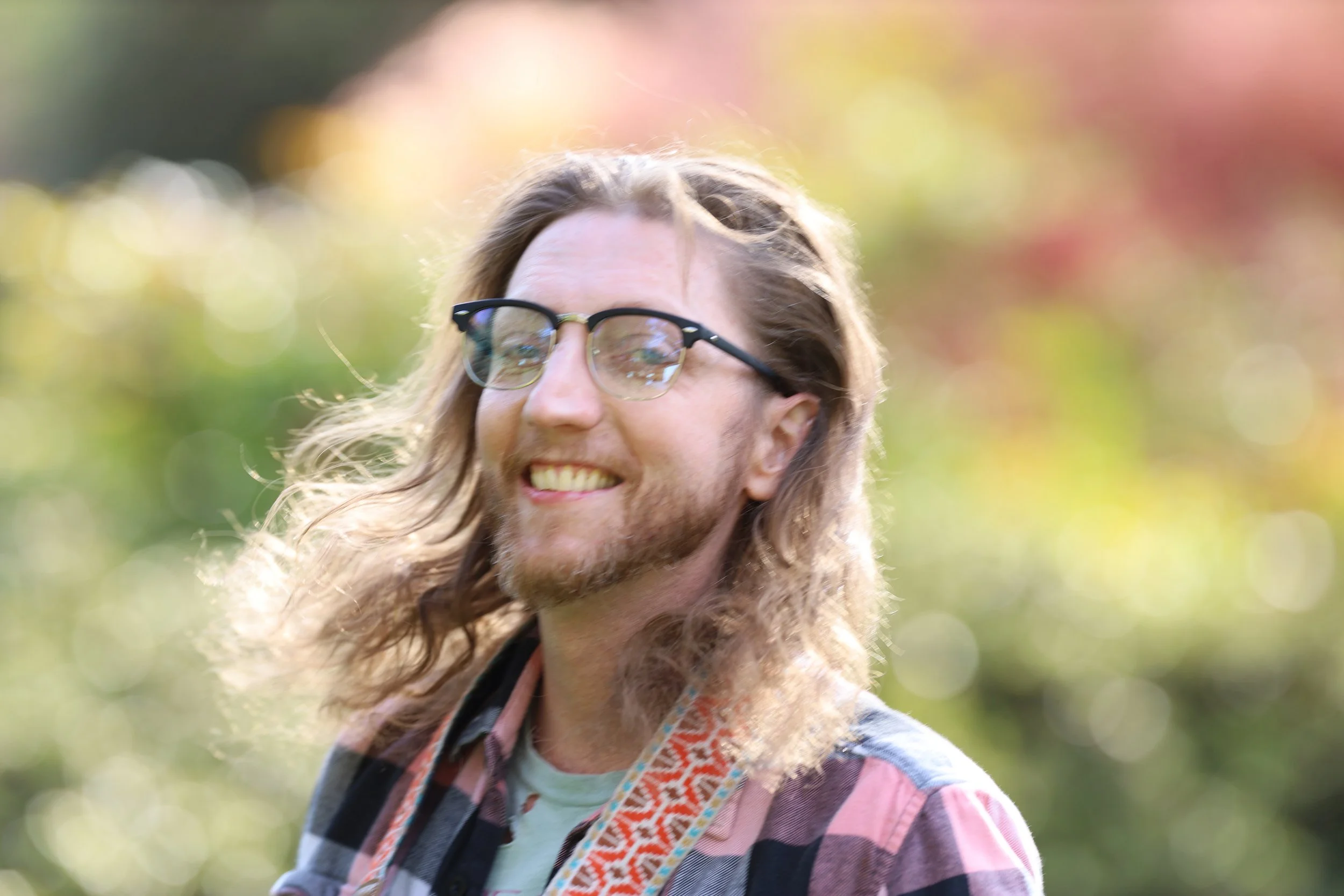 Person with long hair and glasses smiling outdoors