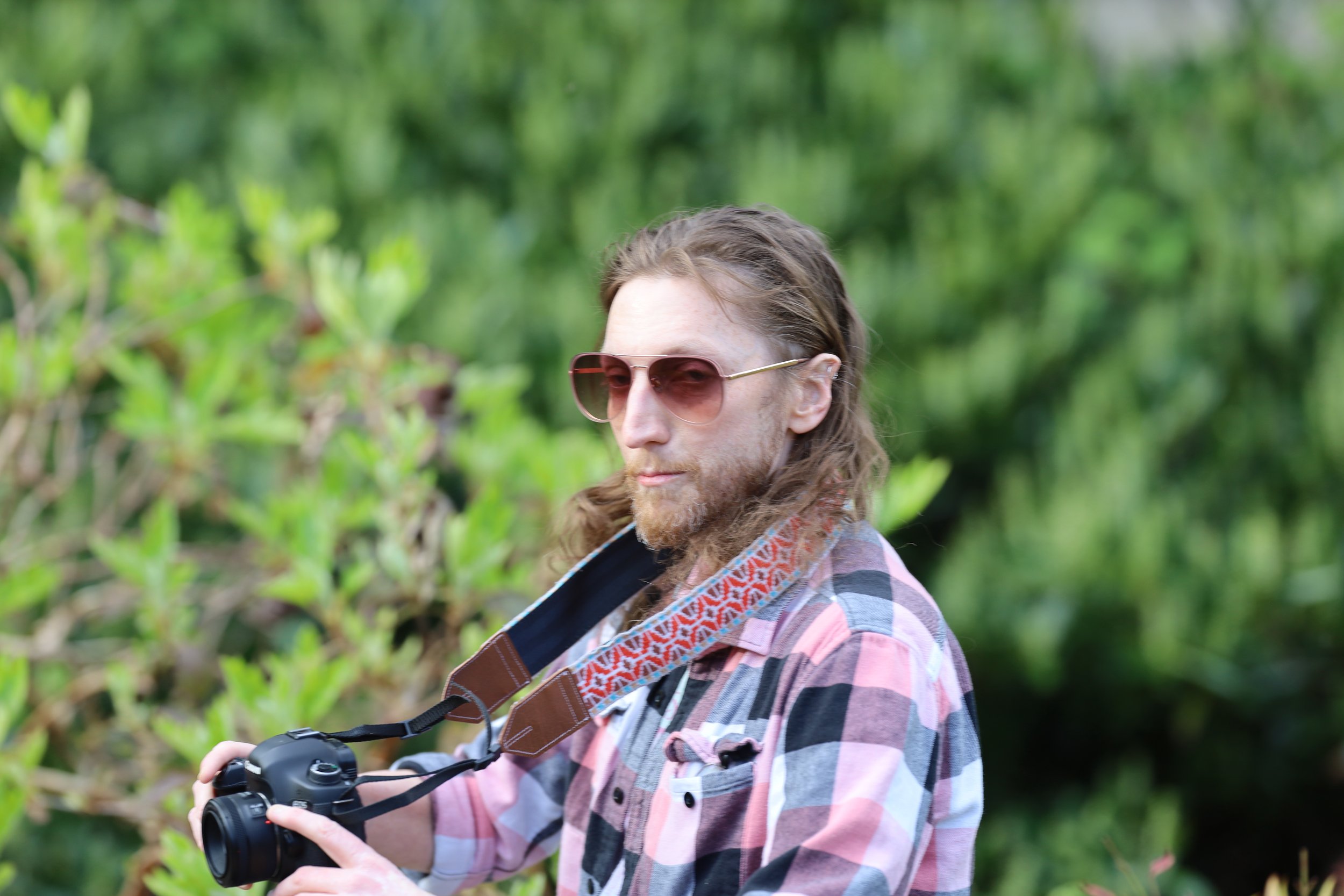 Person with sunglasses holding a camera in a green outdoor setting.