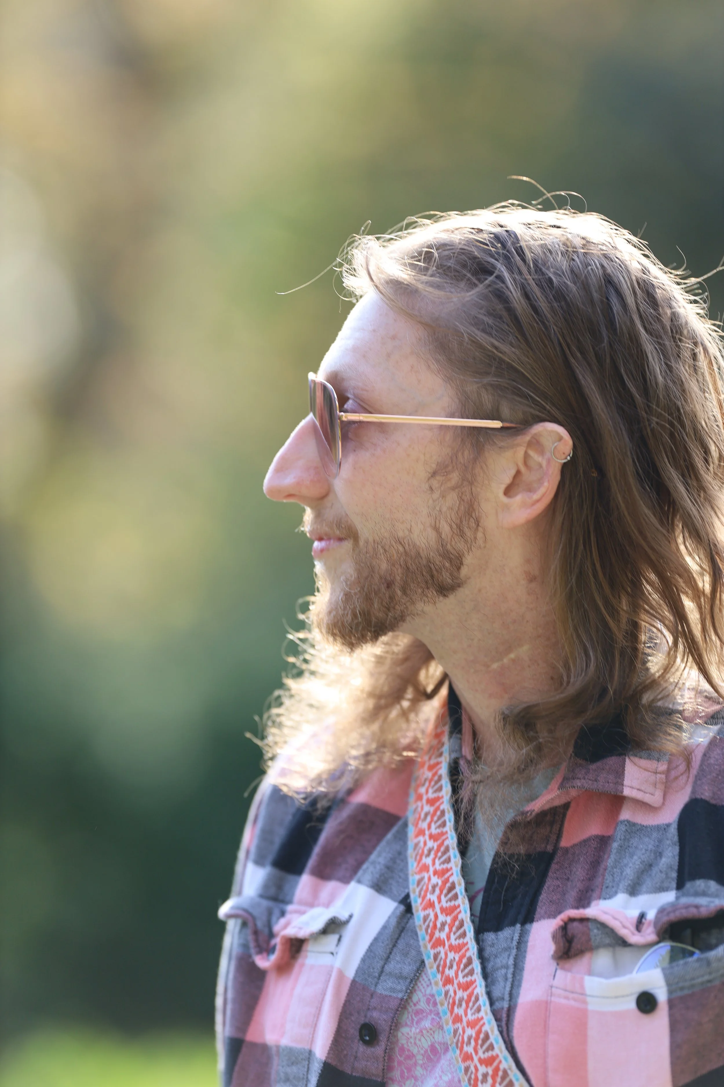 Side profile of a person wearing sunglasses and a plaid shirt outdoors.
