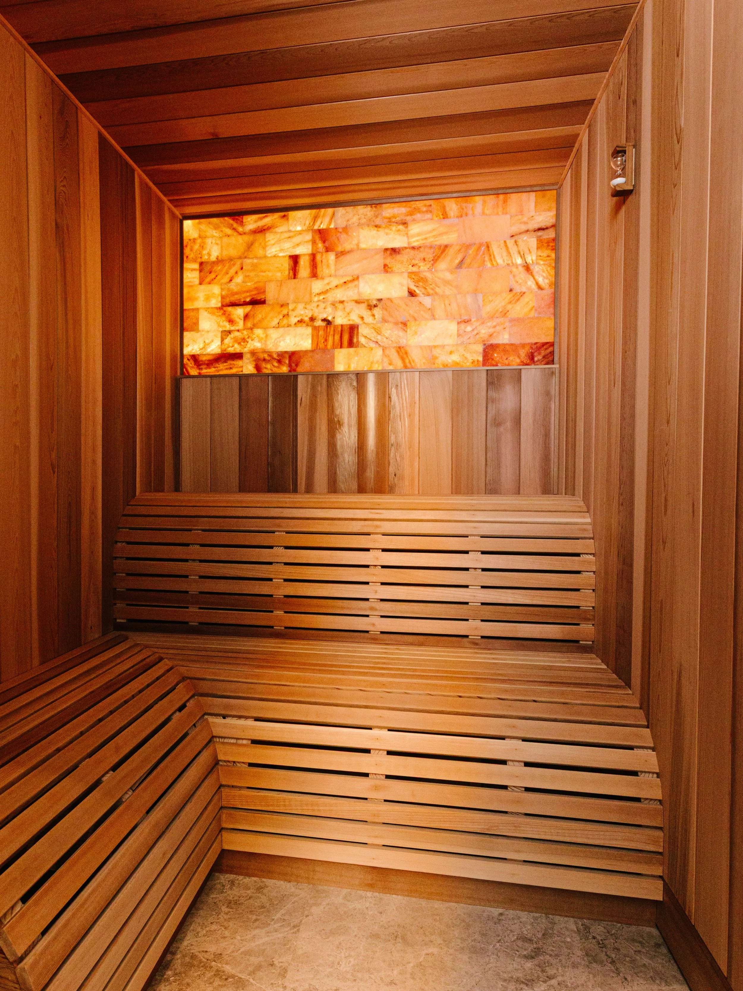We designed this corner of the home to feel like a deep breath. Western red cedar wraps the sauna in warmth, and a backlit Himalayan salt wall glows like a sunset you can sit inside. Just outside, a tucked-away hydration nook waits with chilled water
