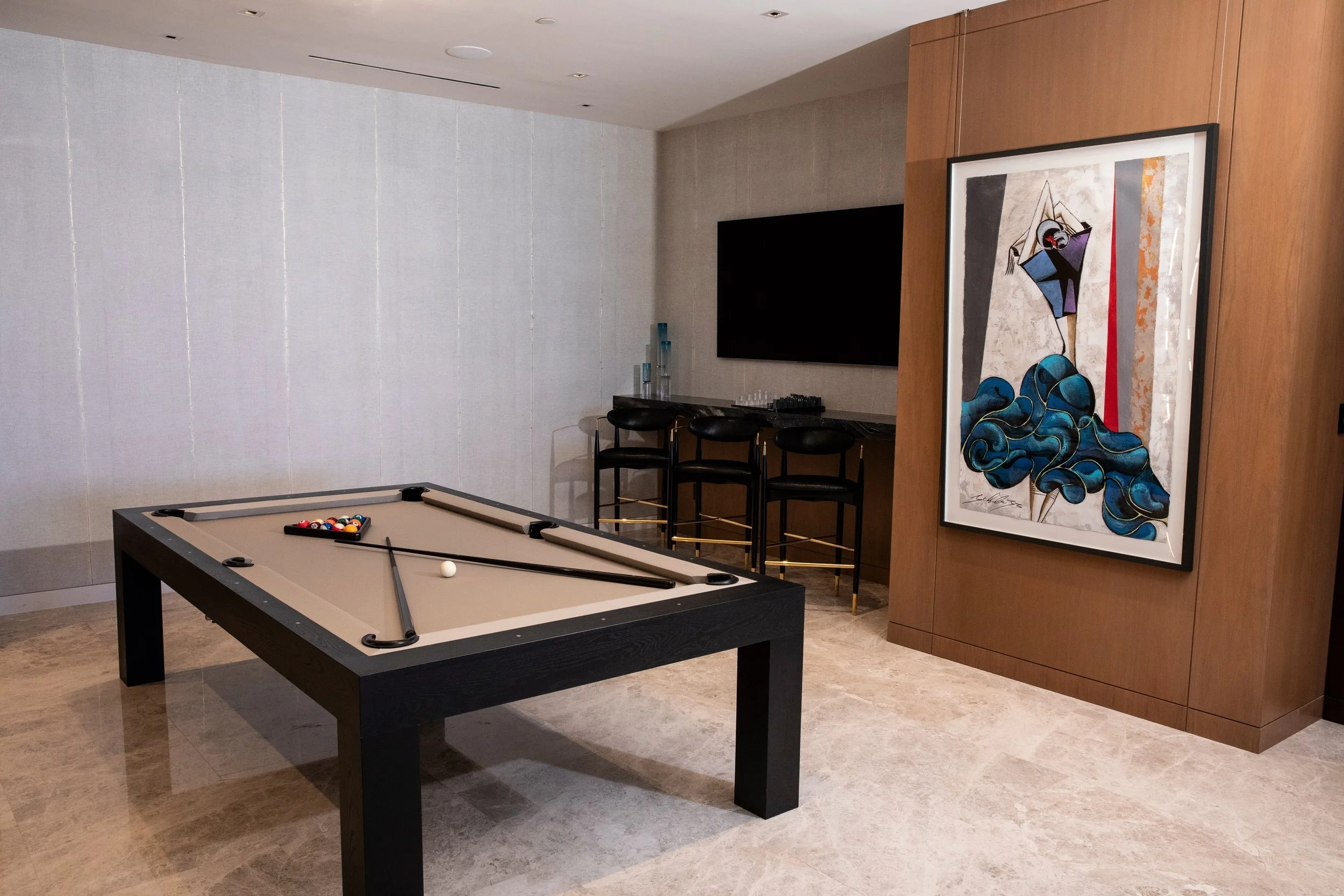 Every great home needs a room with a scoreboard. Ours has a James Perse billiards table dressed in sand-colored felt, a row of leather and brass stools waiting at the bar, and a single oversized work of art that looks like it knows the punchline. Ble