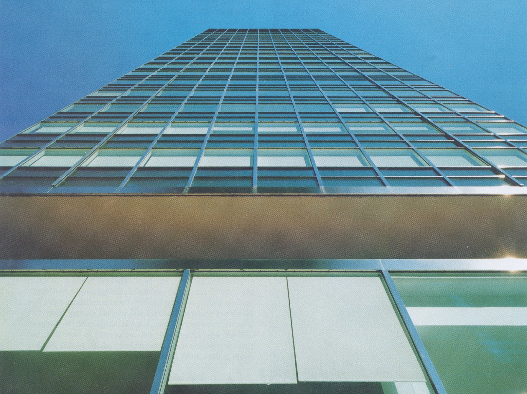 Low-angle view of a modern glass skyscraper with a clear blue sky background.