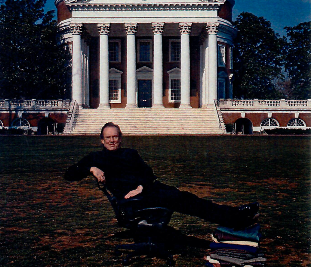 A woman with glasses sitting on a black office chair on a lawn in front of the White House in Washington, D.C. There are some piles of books or papers on the ground beside the chair.