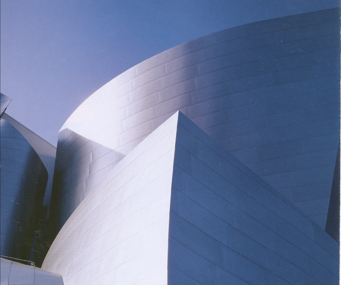 Close-up of modern, curved silver architectural building with sharp edges against a clear blue sky.