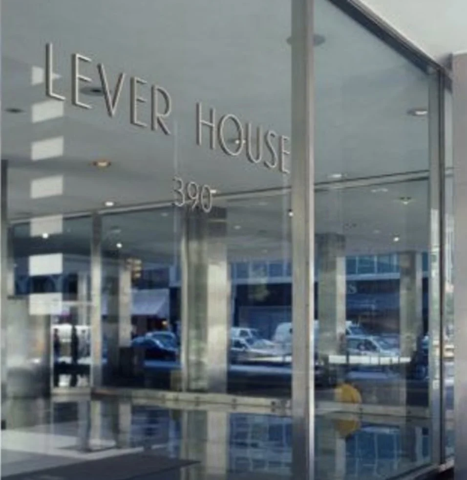 The storefront of a business named 'LEVER HOUSE' with the number '390' displayed, seen through large glass windows reflecting the parking lot and buildings outside.