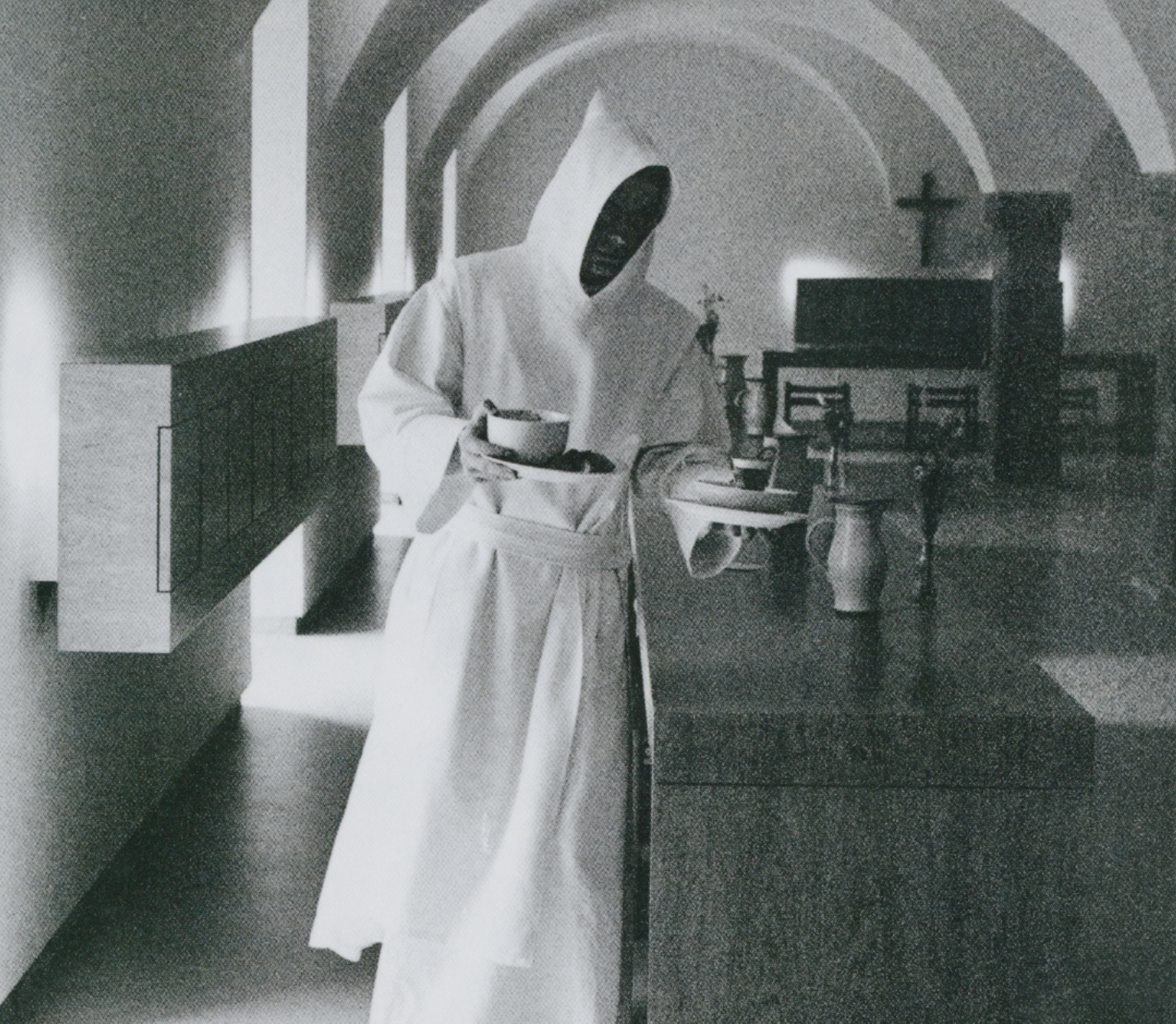 A person dressed in a futuristic white robe with a black mask serving food on a tray in a minimalist interior with arched ceilings and modern furnishings.