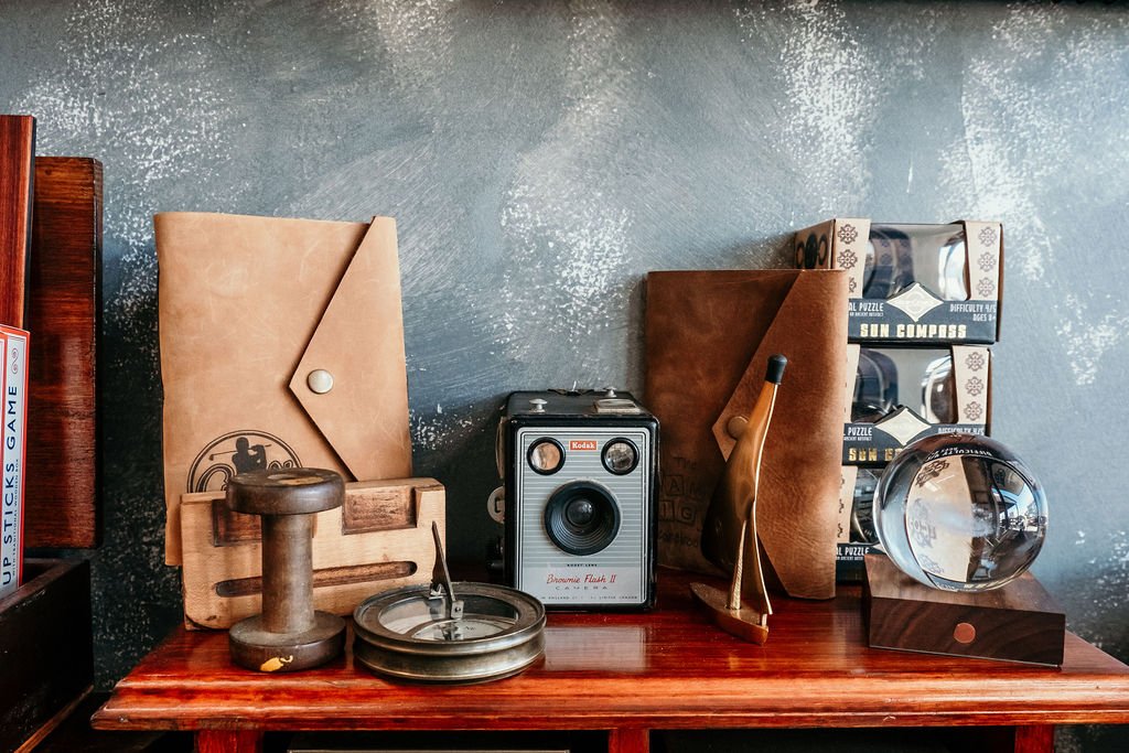 A vintage Kodak camera, several books, decorative objects, and brown leather folders on a wooden surface against a textured blue wall.