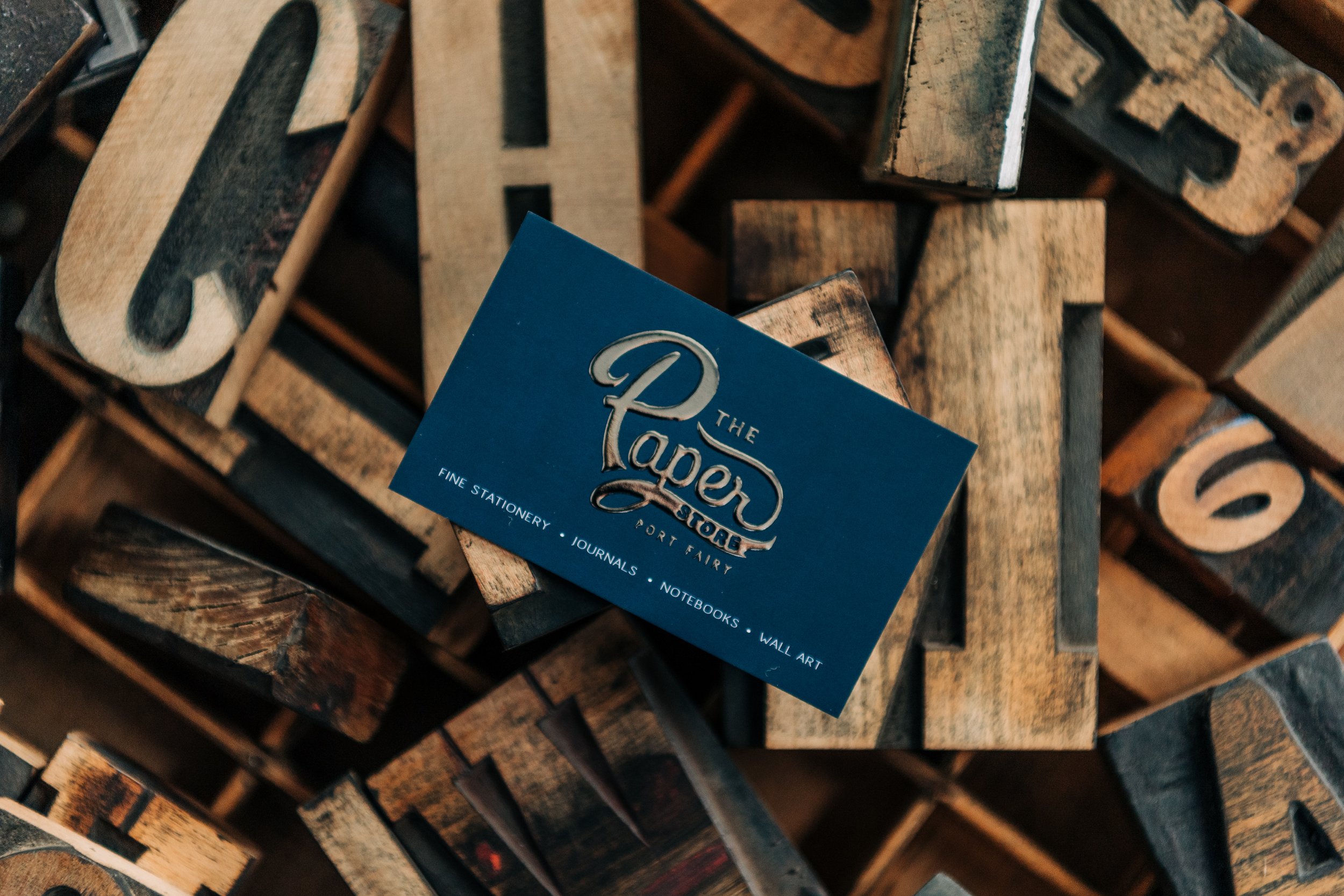 A business card for The Paper Store resting on vintage wooden letterpress blocks.