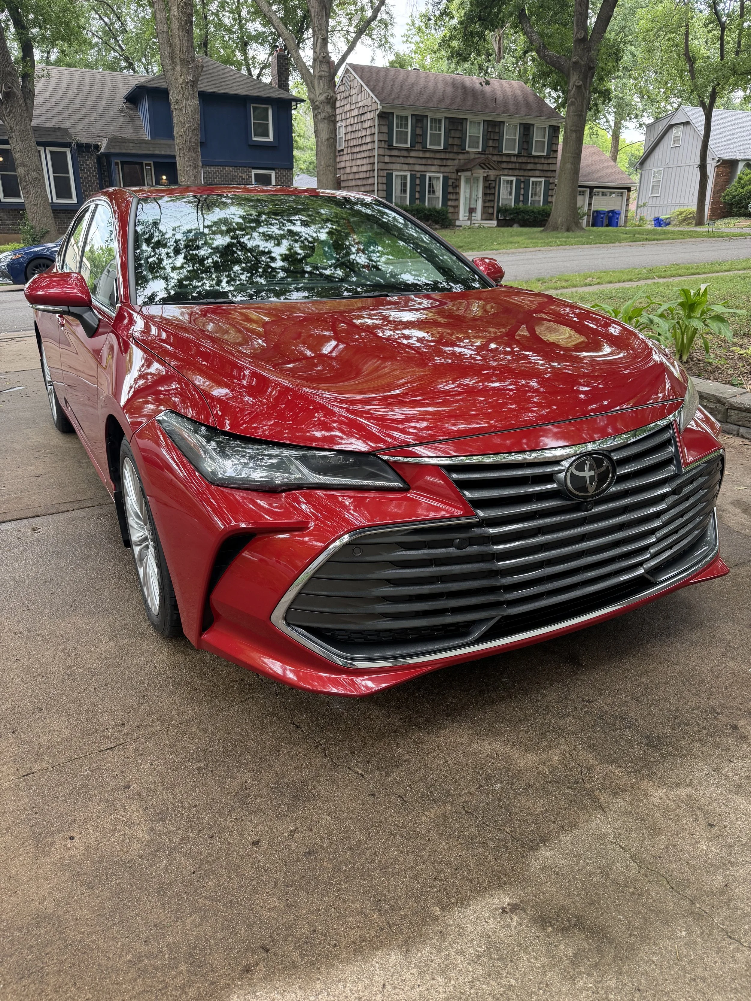 Red Toyota sedan parked on a driveway with houses and trees in the background.