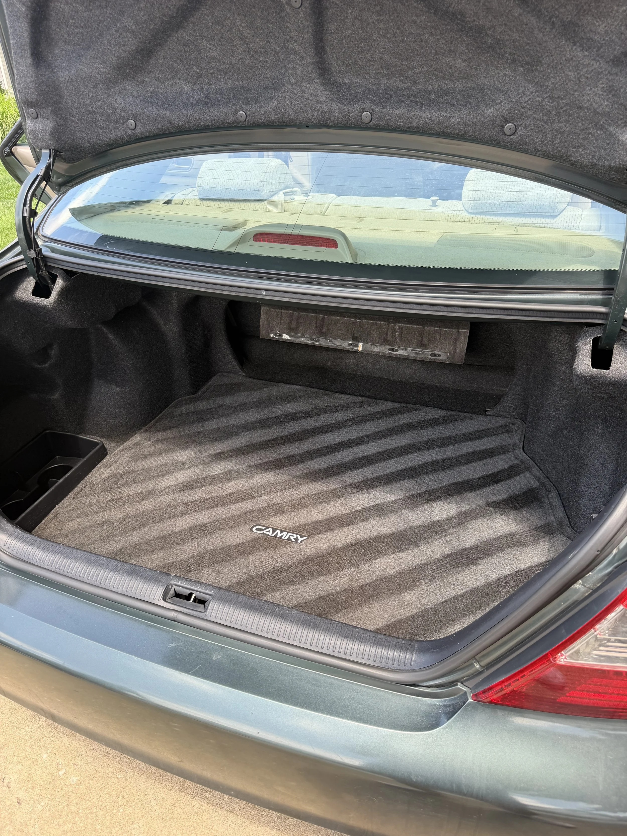 Open trunk of a Toyota Camry, showing a clean black carpeted trunk space with a striped mat and a small storage compartment.