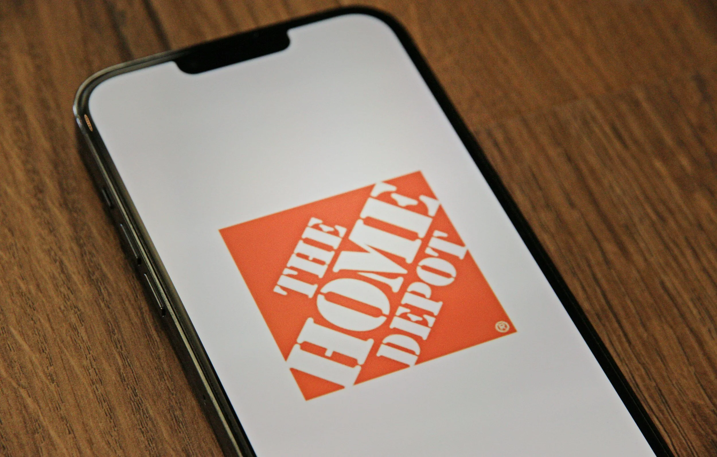 An iPhone displaying The Home Depot logo on its screen, placed on a wooden surface.
