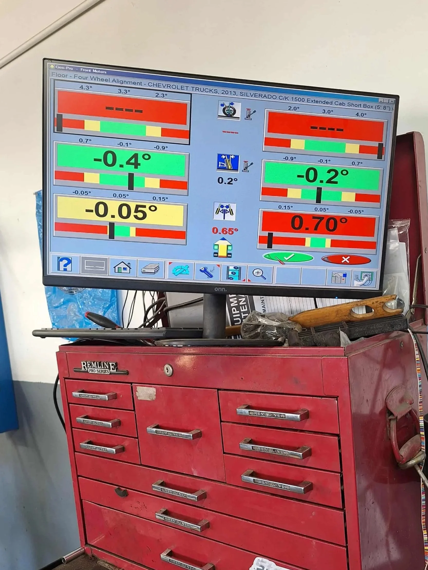 A computer monitor displaying wheel alignment readings for a Chevrolet Silverado truck, with various numerical angles and color-coded indicators, on a red tool chest in an auto repair shop.