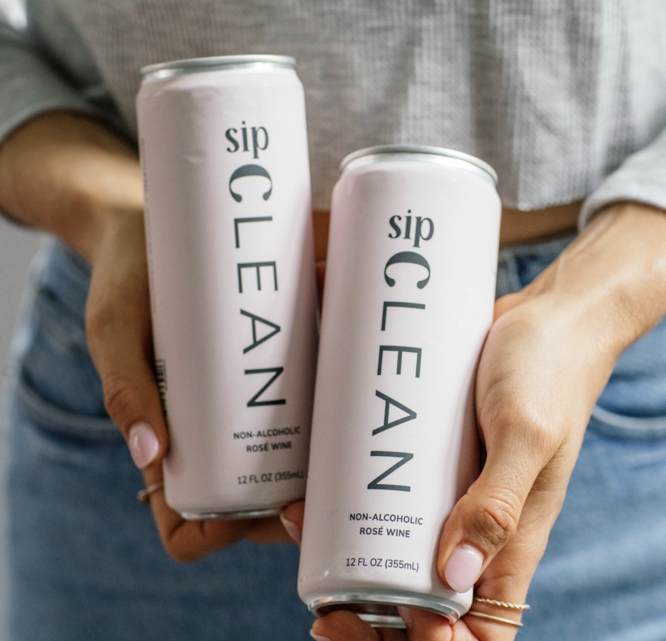 Person holding two cans of non-alcoholic rosé wine with the label 'sip CL EAN'
