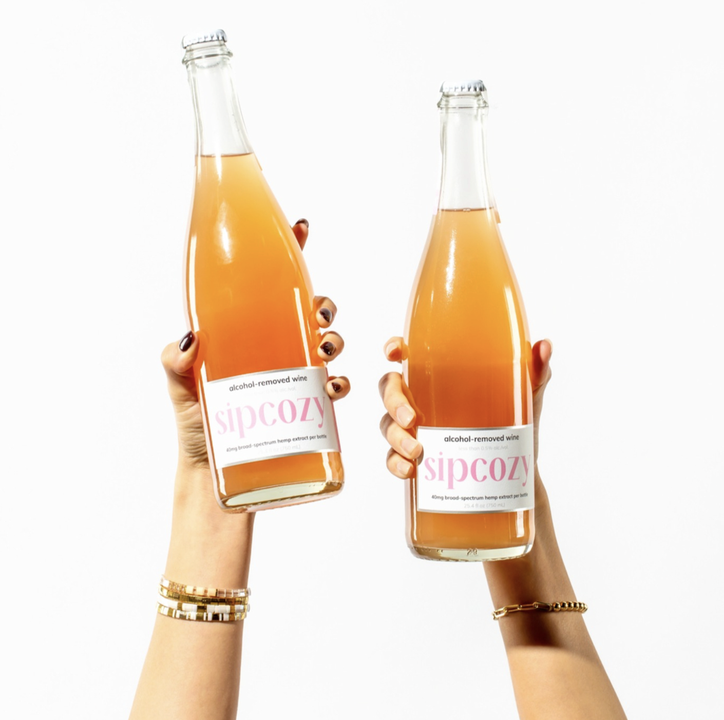 Two hands holding bottles of alcohol-removed wine labeled 'sipcozy' against a white background.