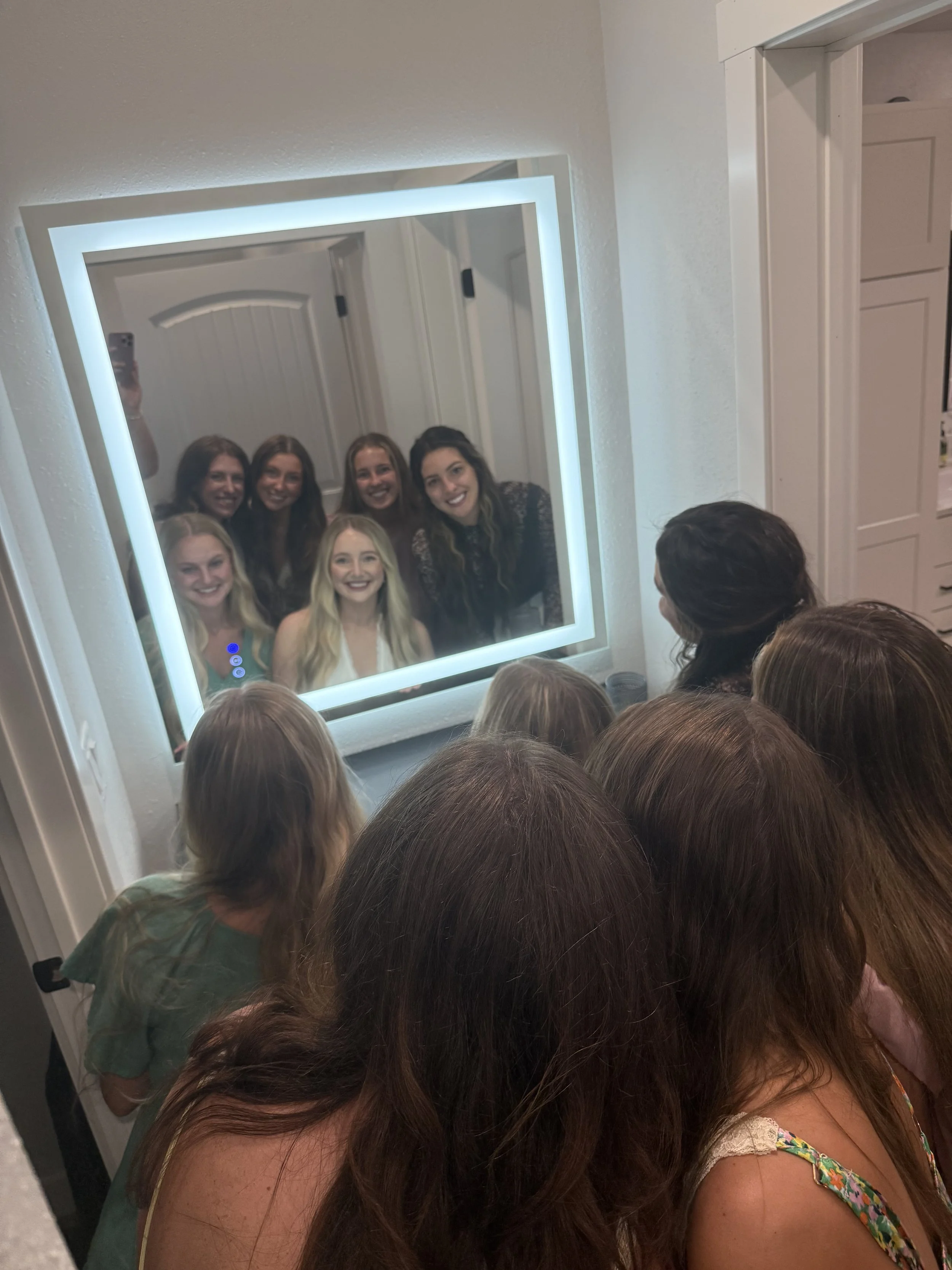 group of women and children looking into a backlit mirror, taking a selfie of their reflection.