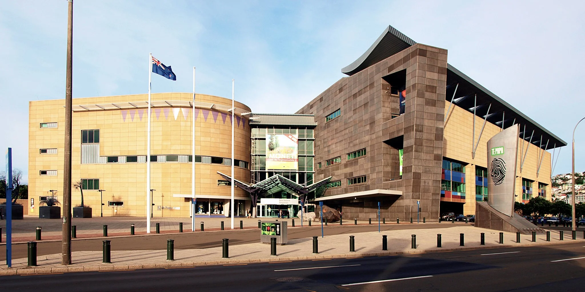 Modern building with curved and angular architecture, flags on poles, parking lot, and clear sky