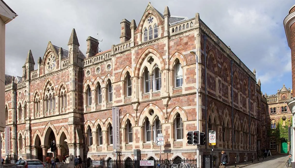 A historic red brick and beige stone building with pointed arch windows and decorative architectural details, situated on a city street corner.
